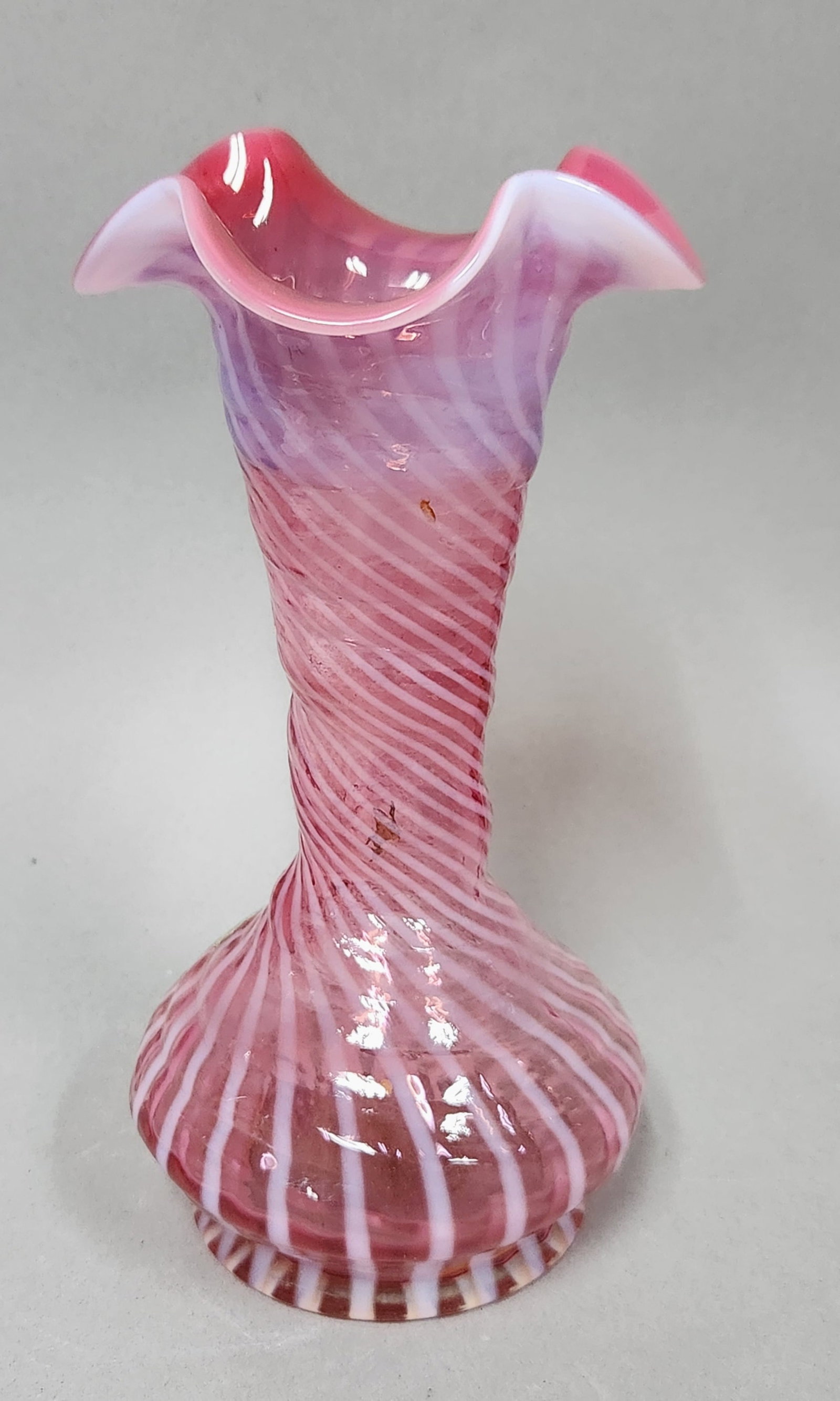 Fenton Cranberry Opalescent Vase: This Fenton Art Glass vase is crafted from cranberry opalescent glass featuring a spiral swirl optic pattern. Height: 8.5 inches Base diameter: 3.25 inches. The vase is in excellent condition with no