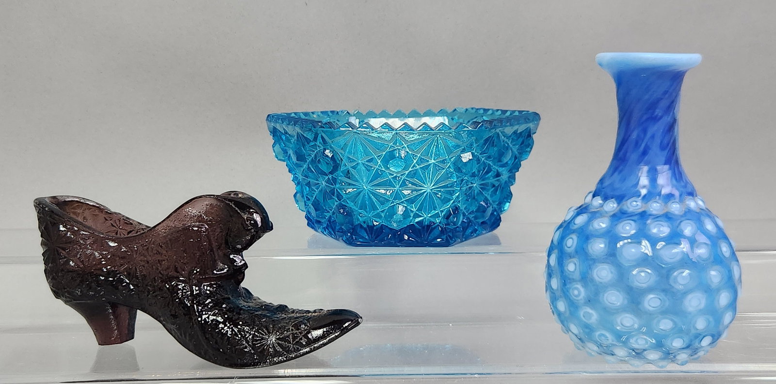 Decorative American Glass Items: This lot consists of a mold-pressed glass cat in boot figurine and a blue hexagonal bowl, both decorated with a daisy and button pattern. The third item is a blue opalescent bud vase featuring a spira