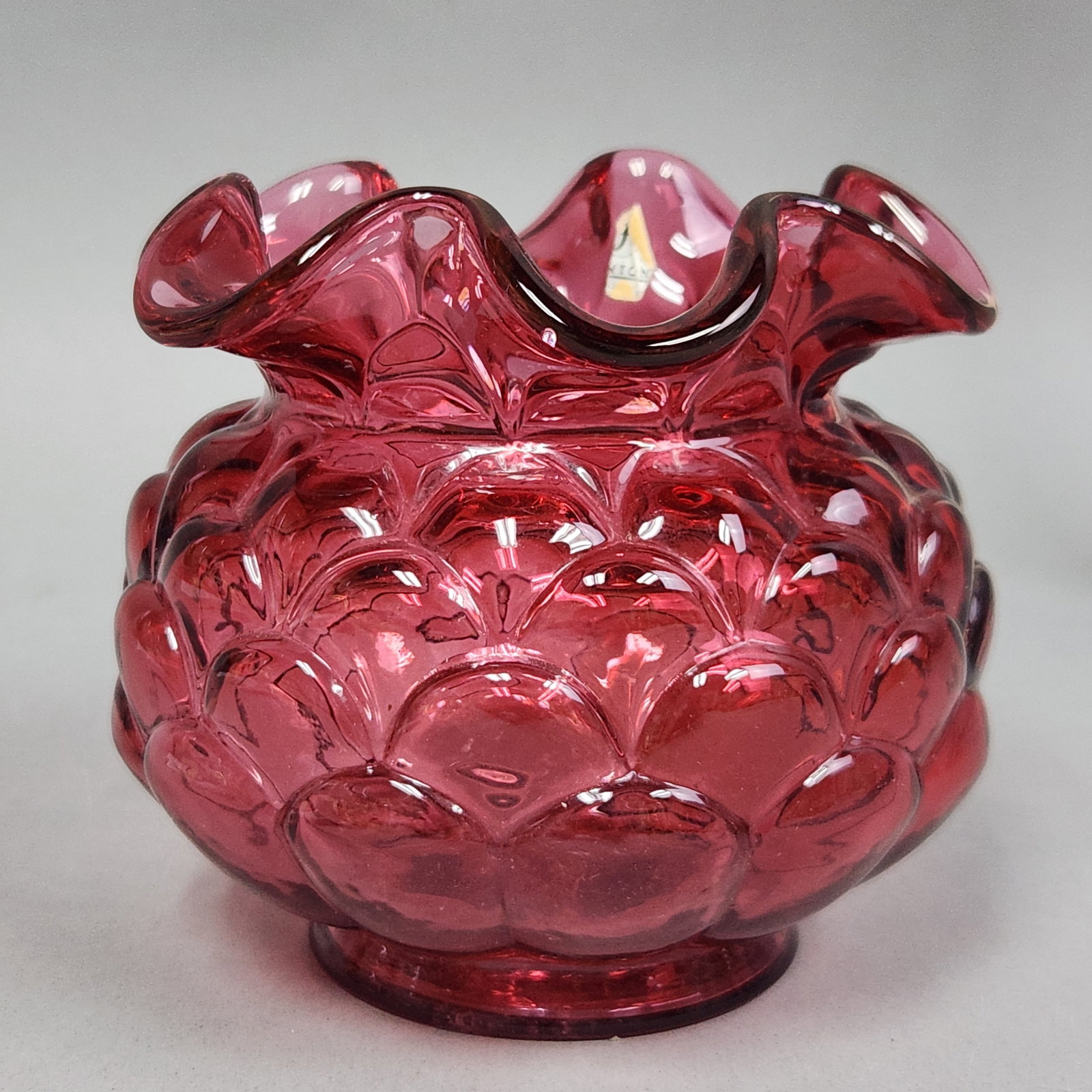 Fenton Cranberry Glass Rose Bowl: This Fenton cranberry glass rose bowl features a mold-blown body with an overall bubble texture and a hand-crimped, ruffled rim. A partial original Fenton gold foil label is present on the interior ri