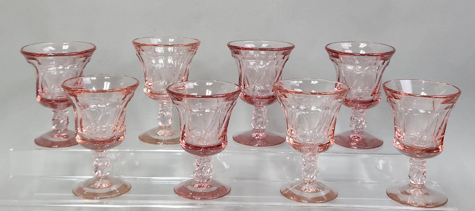 Fostoria Jamestown Pink Glasses: A set of eight Fostoria Jamestown pink footed glasses featuring flared bowls with vertical optic ribbing. Height: 4 1/4 inchesThe set is in very good vintage condition without chips, cracks, or