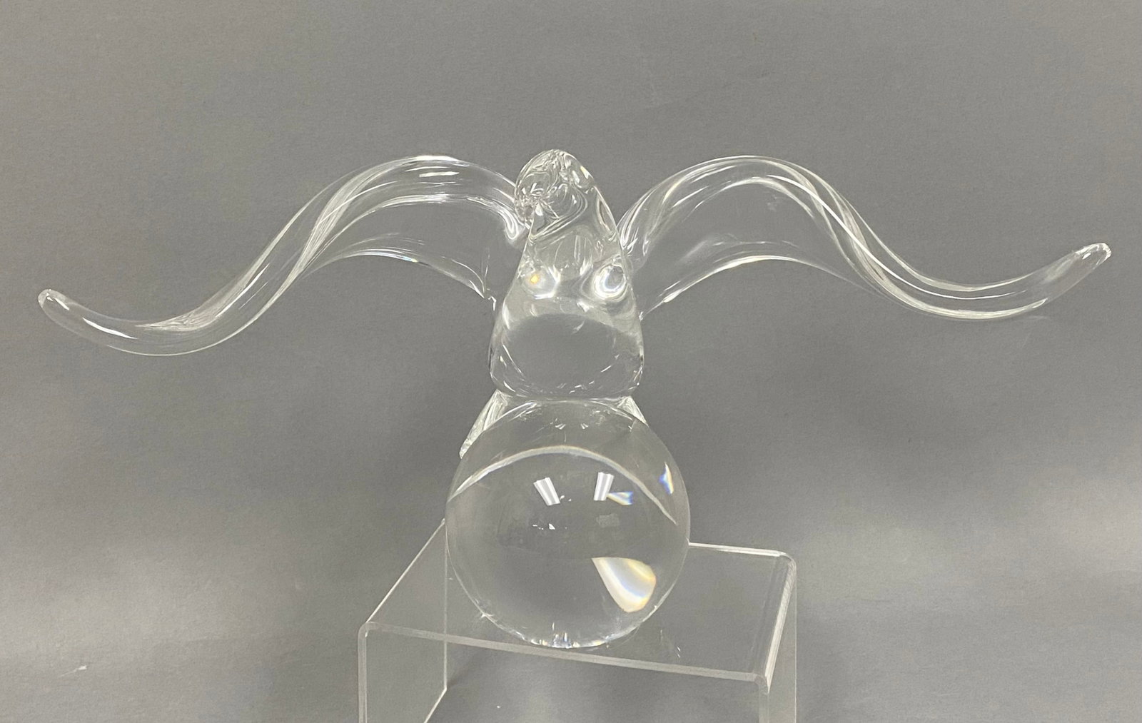 Steuben Crystal Eagle on Ball: A Steuben clear lead crystal sculpture depicting a stylized eagle in flight perched atop a solid spherical base. The piece features arched, outspread wings and is executed in a minimalist, fluid style