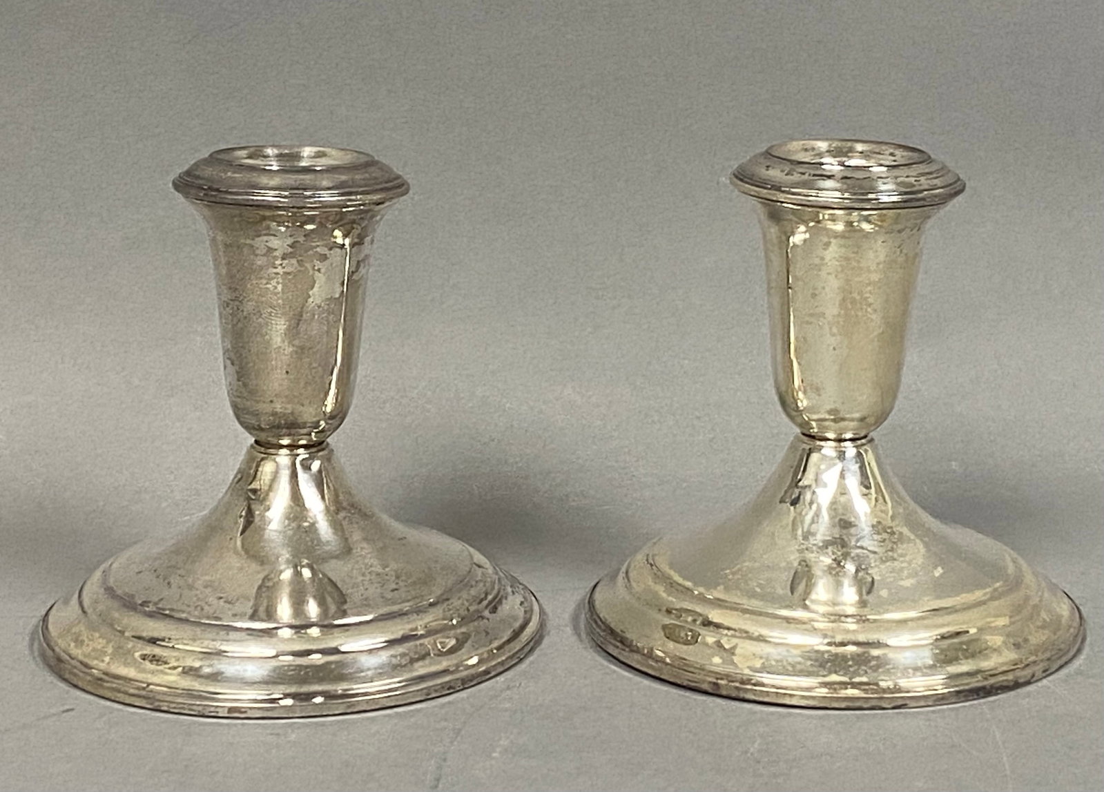 Duchin Creation Sterling Weighted Candlesticks: A pair of matching short weighted candlesticks manufactured by Duchin Creation. Each piece features a flared rim above a tapering bell-shaped stem, resting on a wide, stepped circular base in a