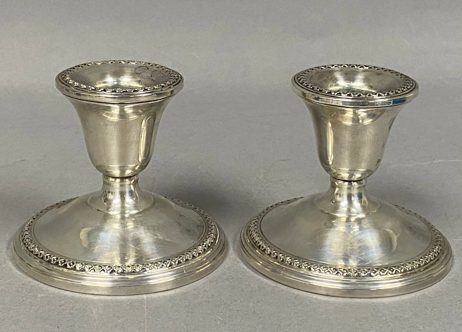 F. B. Rogers Sterling Beaded Candlesticks: A matched pair of American sterling weighted candlesticks by the F. B. Rogers Silver Co. featuring a classic low-profile design. Each piece is constructed with a bell-shaped candle cup and flared rim