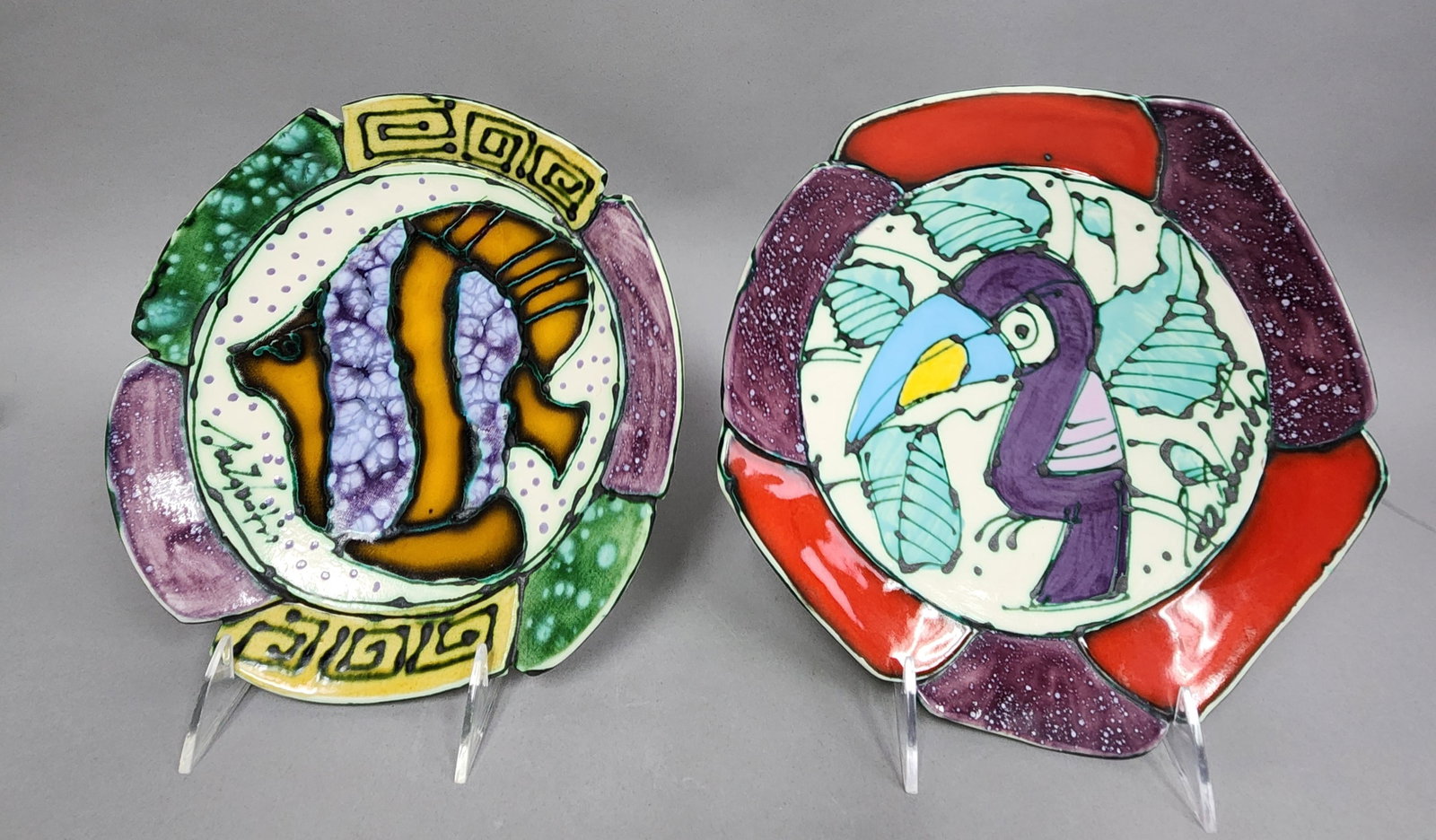 Glazed Ceramic Tropical Plates: This set includes two handcrafted studio pottery plates featuring vibrant tropical motifs in the style of artist Juozas Rasa Saldaitis. Signature is illegible. Diameter: 9 inches The plates are in exc