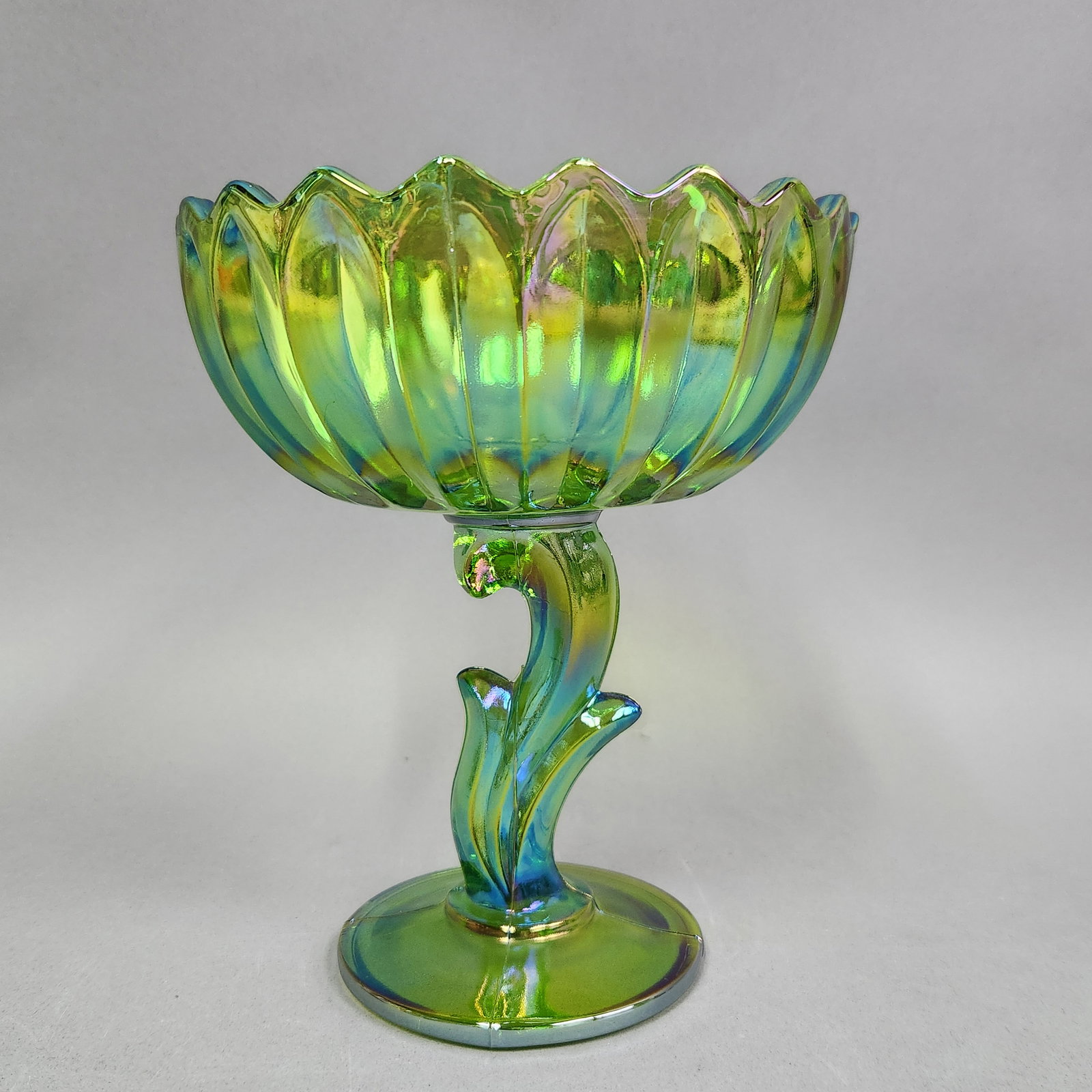 Indiana Glass Carnival Lotus Blossom Compote: An Indiana Glass pedestal compote featuring an iridescent green finish with metallic highlights of blue, gold, and purple. Height: 6 inches The compote is in excellent vintage condition. There are no 