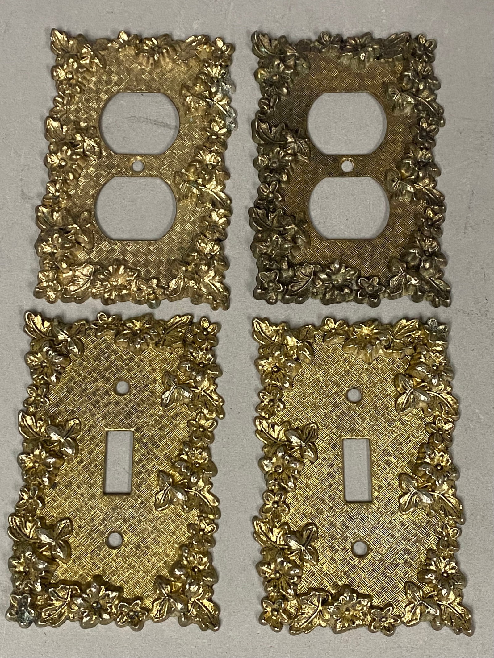 American Tack & Hardware Brass-Plated Ornate Wall Plates: A set of four vintage cast metal wall plates produced by the American Tack & Hardware Co. in the late 1960s. The group consists of two covers for single-toggle light switches and two covers for standa
