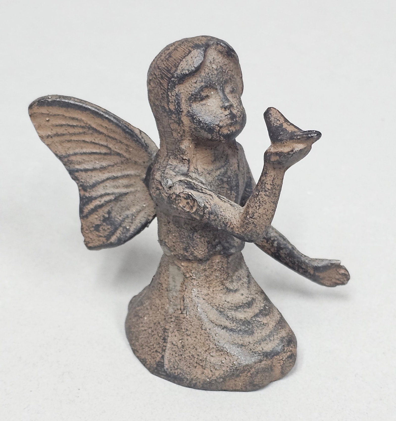 Cast Iron Kneeling Fairy Figurine: A small decorative cast iron figurine depicting a kneeling winged fairy. The figure is posed with her right hand raised, holding a small bird, while her left arm extends downward and back. The base