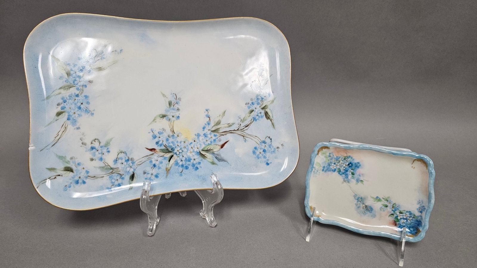 Limoges Porcelain Hand-Painted Forget-Me-Not Trays: Two Limoges porcelain trays featuring hand-painted floral decorations. The larger rectangular tray has a curved scalloped rim with a gilded edge and is decorated with branches of blue forget-me-not fl