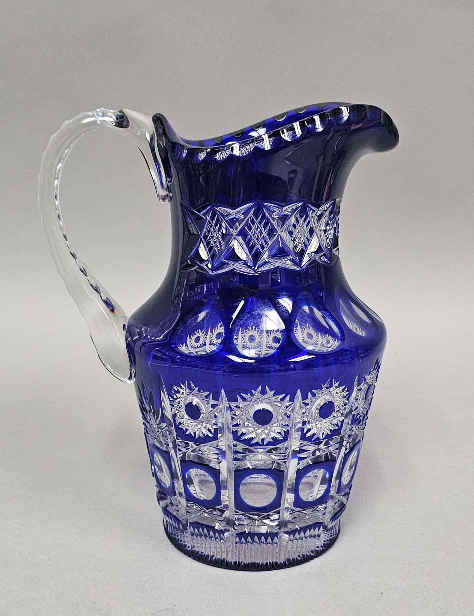 Tisch Berchtesgaden Cobalt Cut to Clear Crystal Pitcher: A German cased crystal water pitcher featuring deep cobalt blue glass cut to clear in an elaborate geometric pattern. The body is decorated with starburst motifs set within a grid of circular