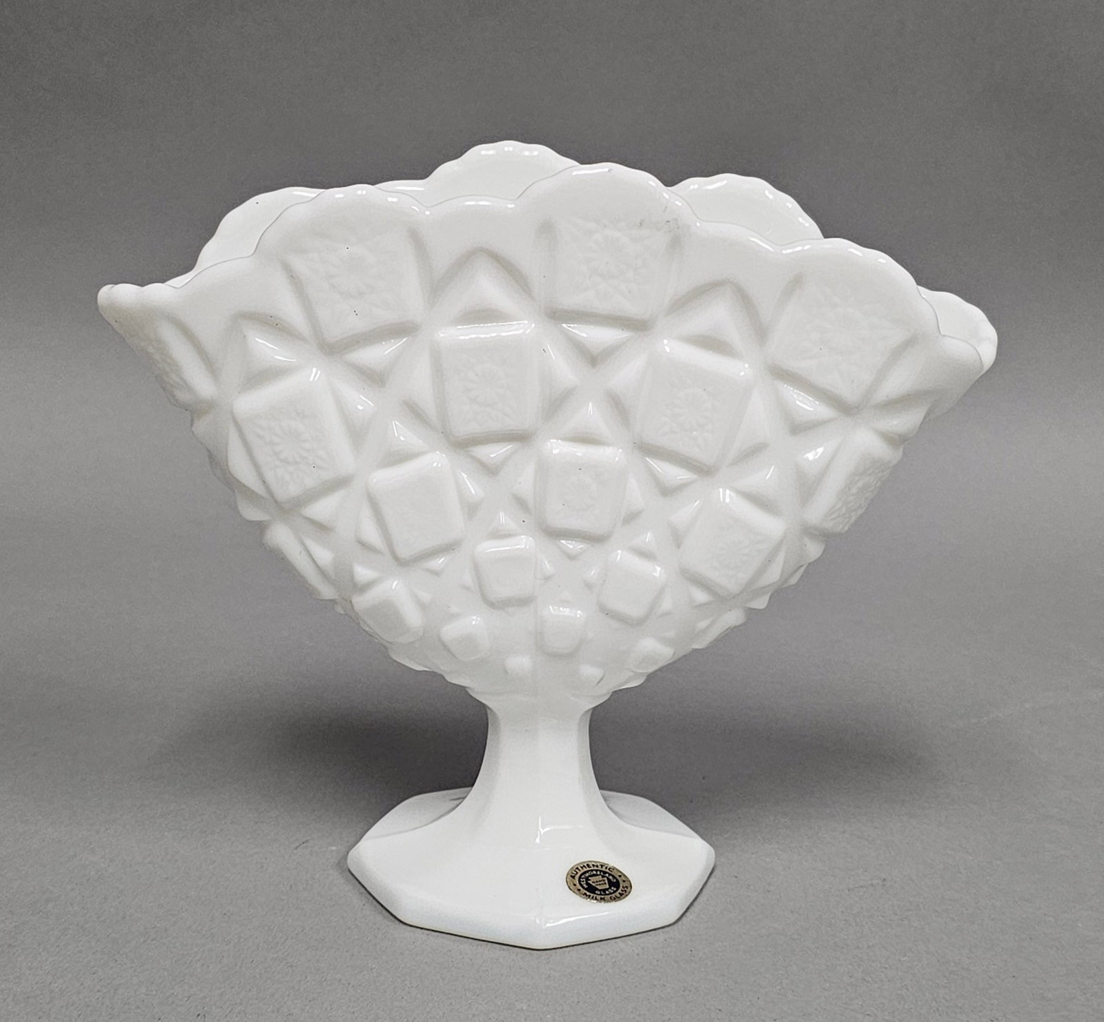 Westmoreland Milk Glass Fan Vase: A vintage milk glass fan-shaped vase produced by the Westmoreland Glass Company. A circular gold and black foil sticker is adhered to the base and reads AUTHENTIC WESTMORELAND GLASS HAND MADE MILK