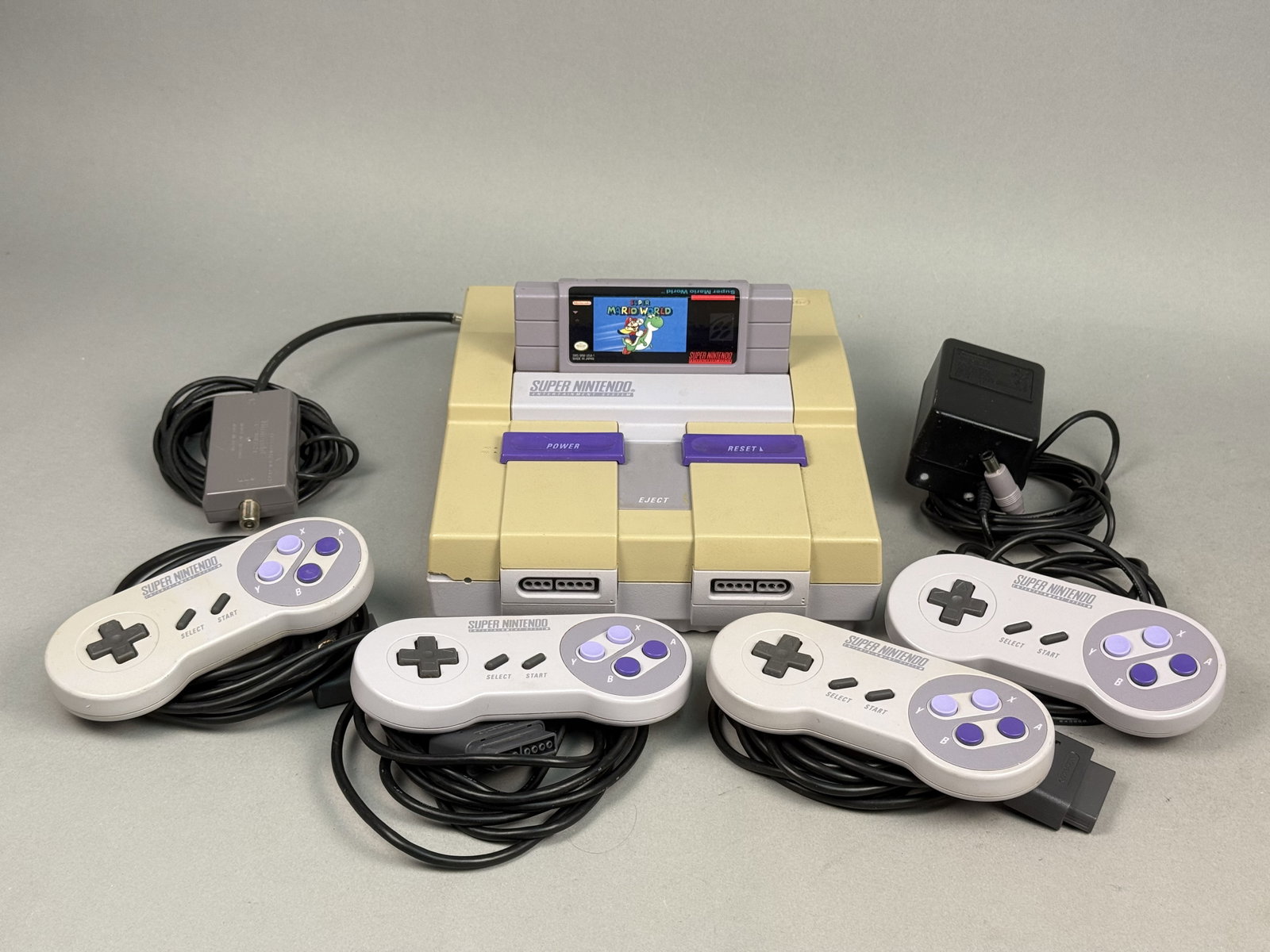 Nintendo Super Nintendo SNES Bundle: This Nintendo Super Nintendo Entertainment System (SNES) bundle features a model SNS-001 console accompanied by a collection of four original wired controllers. The set includes a model SNS-002 AC