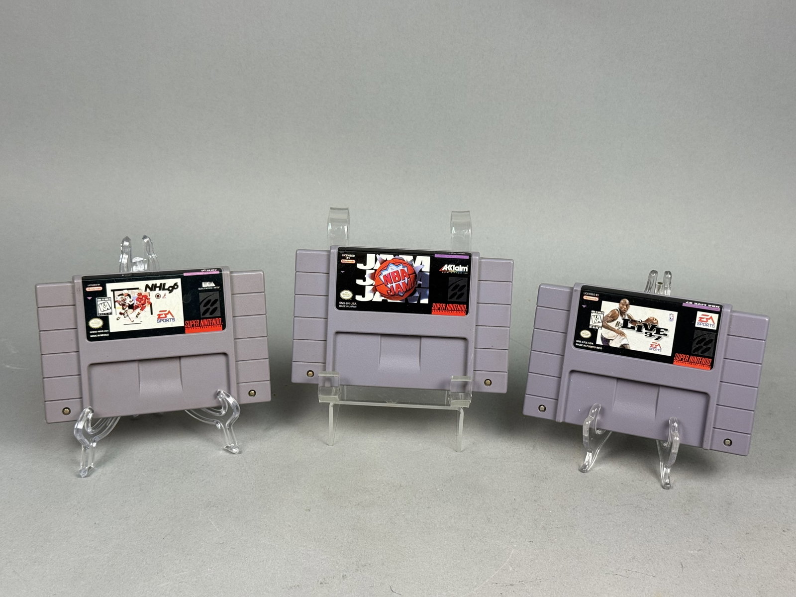 Three SNES Sports Game Cartridges: A trio of Super Nintendo Entertainment System cartridges featuring titles from Electronic Arts and Acclaim Entertainment. This lot consists of NHL '96, NBA Live 97, and NBA Jam, each constructed from