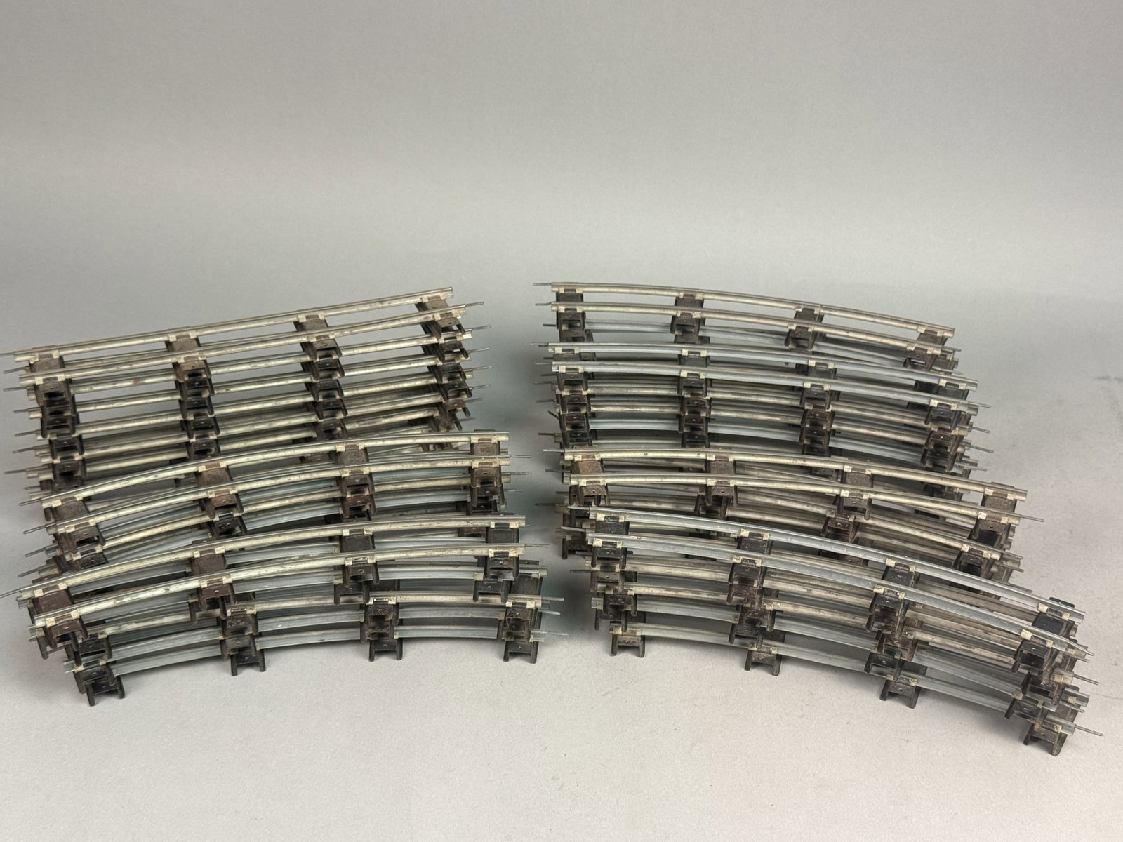 Assortment of O-Gauge Railroad Track: An assortment of approximately 35 to 40 individual sections of O-gauge three-rail model railroad track featuring tubular steel rails on blackened metal ties. The collection includes both straight and