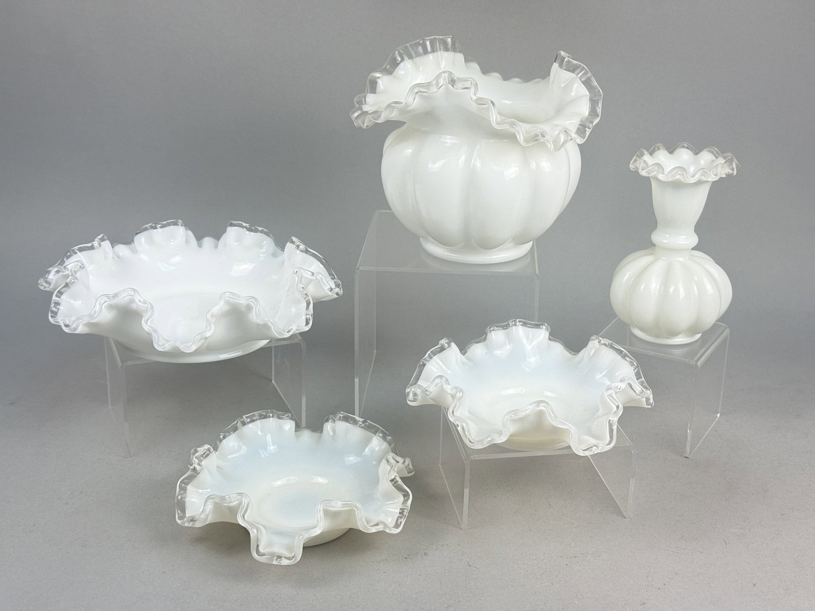 Fenton Silver Crest Milk Glass Set: A five-piece collection of Fenton Silver Crest milk glass featuring opaque white bodies with clear, double-crimped crystal rims. The set includes a large ruffled bowl, a bulbous vase with a ruffled