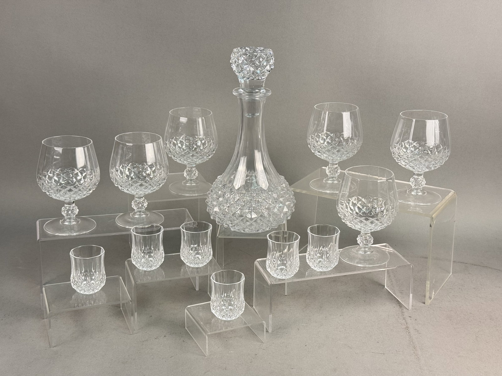 Cristal d'Arques Longchamp Decanter Set: This drinkware set is crafted from clear cut crystal featuring a matching diamond and fluted motif. The set comprises one decanter with a faceted ball stopper, six footed brandy snifters, and six foot