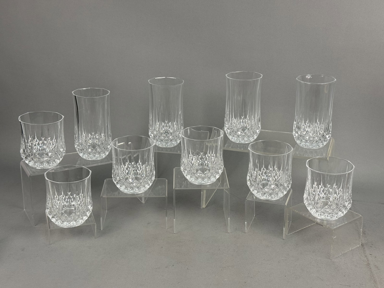 Cristal d'Arques Longchamp Crystal Glassware Set: A set of ten Cristal d'Arques crystal tumblers in the Longchamp pattern. The group includes four highball glasses and six rocks glasses featuring deep diamond-cut bases and vertical mitered flutes. Ea