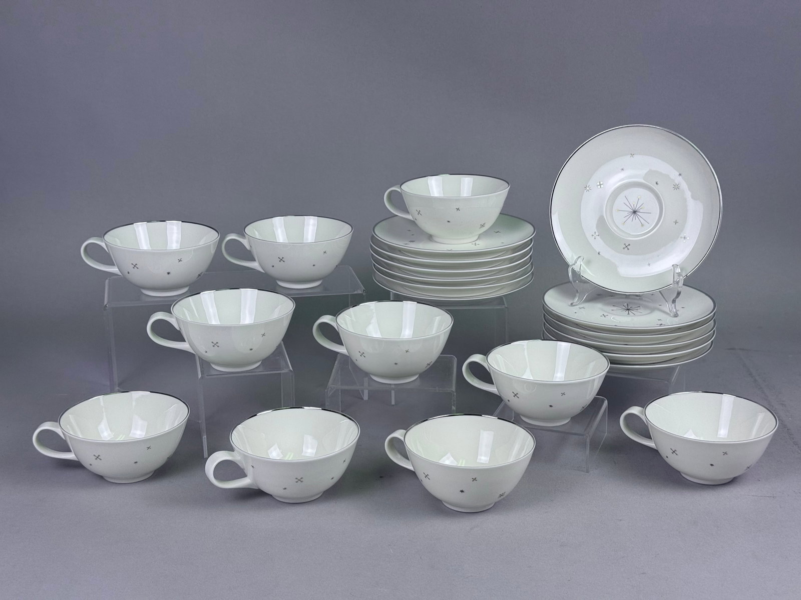 Syracuse Evening Star Porcelain Cups & Saucers: A set of teacups and saucers in the Evening Star pattern by Syracuse China. The fine porcelain bodies are finished in a cream-white glaze and decorated with a Mid-Century Modern atomic motif featuring