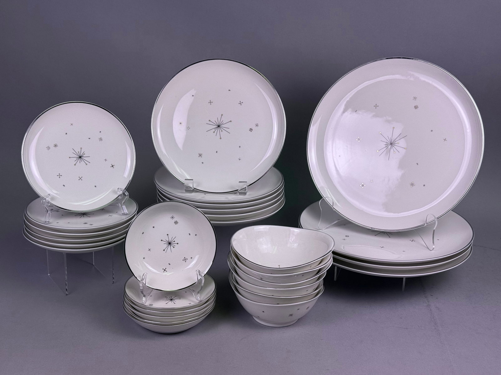 35pc Atomic Starburst Porcelain Dinnerware: A thirty-five piece partial porcelain dinner service featuring a mid-century modern atomic starburst motif. The decoration consists of a central black-lined starburst accented with metallic gold-tone 