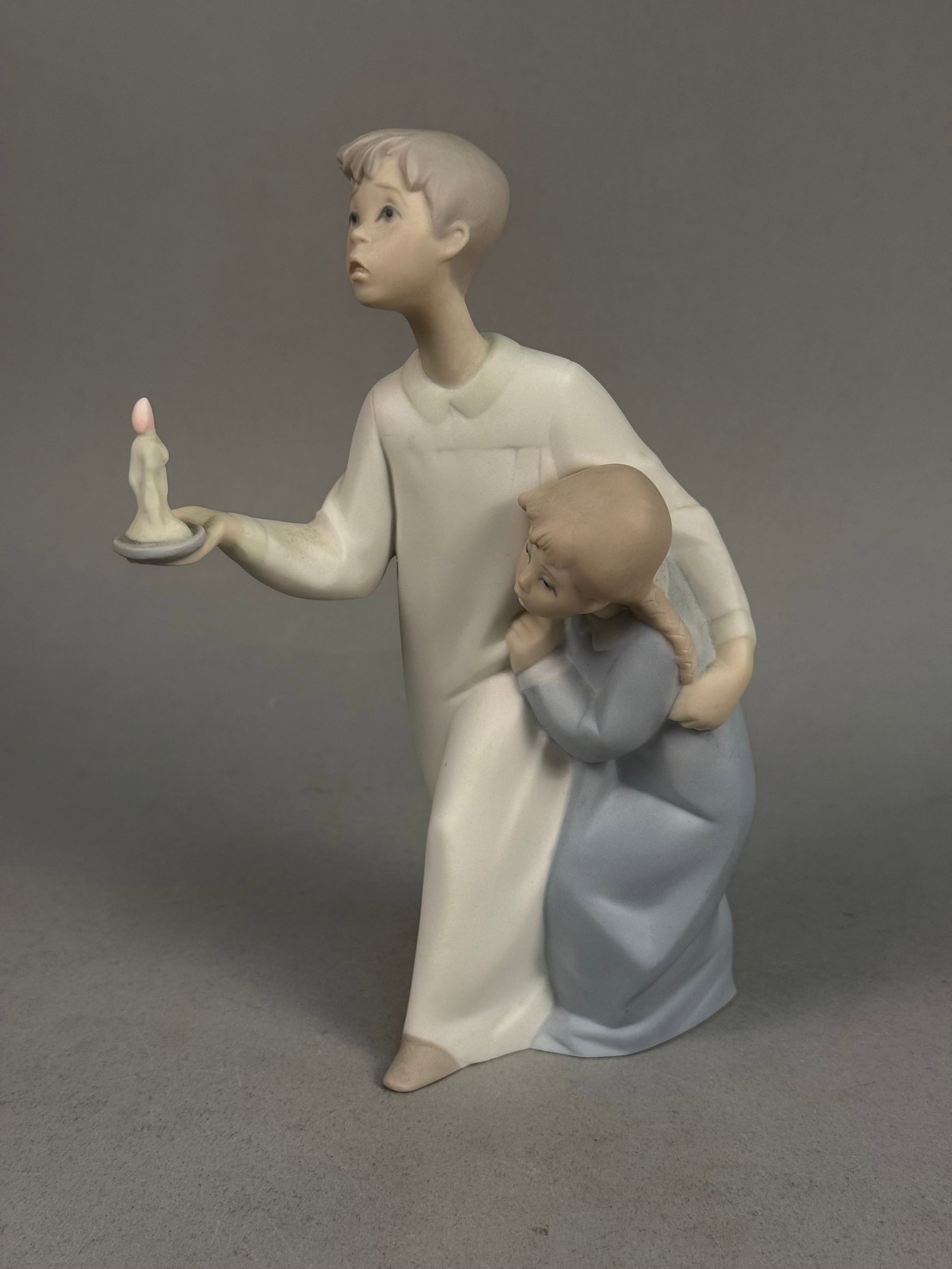 Lladro Matte Porcelain Children & Candle Figurine: A vintage matte-finish porcelain figurine produced by Lladro in Spain, depicting two children in nightclothes. The scene features an older boy in a long white nightgown holding a candle while a