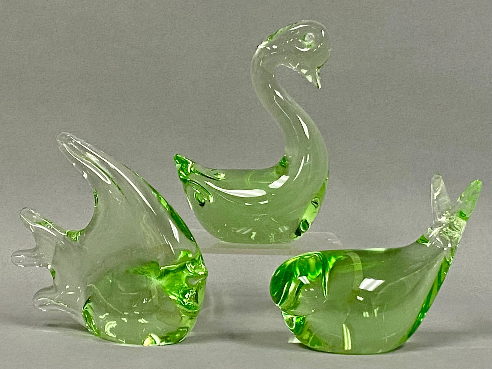 Trio of Green Art Glass Figurines: This trio of hand-blown art glass figurines includes a swan, a stylized tropical fish, and a bird. Each piece is formed from transparent light green glass containing internal swirls of vibrant lime
