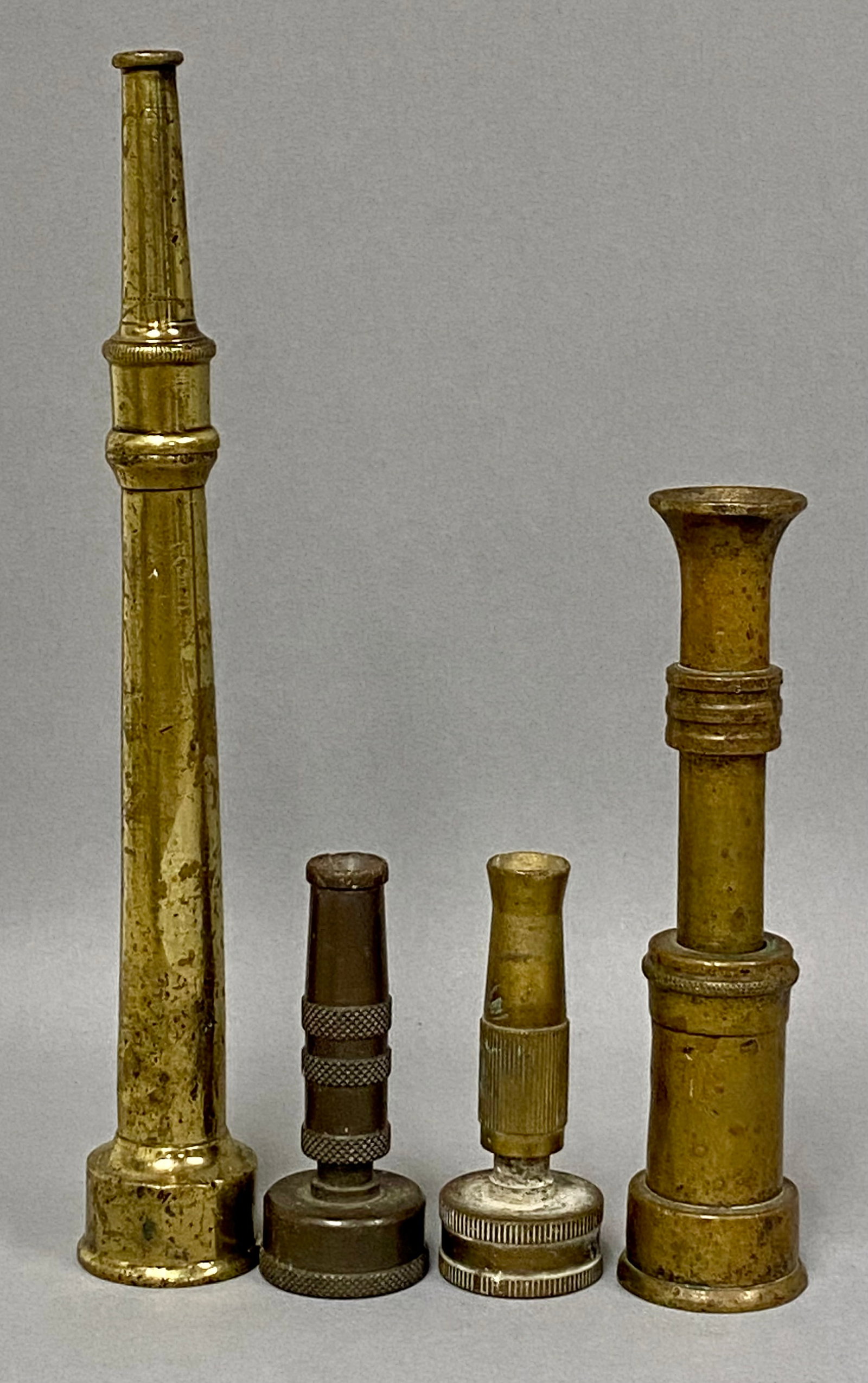 Collection of Vintage Brass Hose Nozzles: An assortment of four vintage brass water hose nozzles featuring fire-style tapered forms and adjustable garden-style grips. Two nozzles are stamped Elkhart Brass Manufacturing Company (marked E.B.P