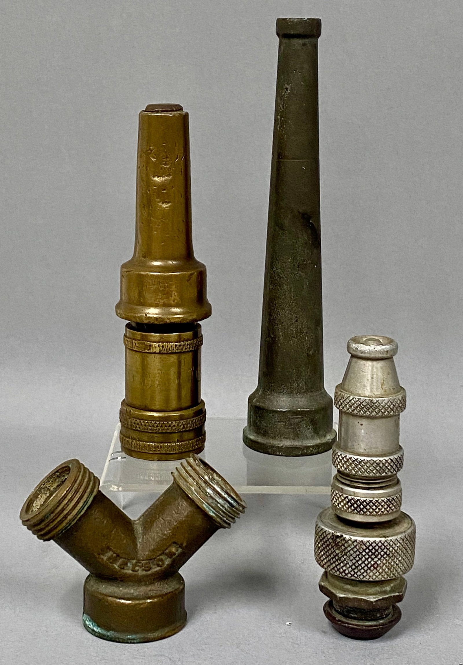 Vintage Metal Hose Fittings Collection: A collection of vintage metal garden hose equipment including a Nelson brand Y-splitter and multiple adjustable spray nozzles. The pieces are constructed from cast brass, bronze, and silver-toned