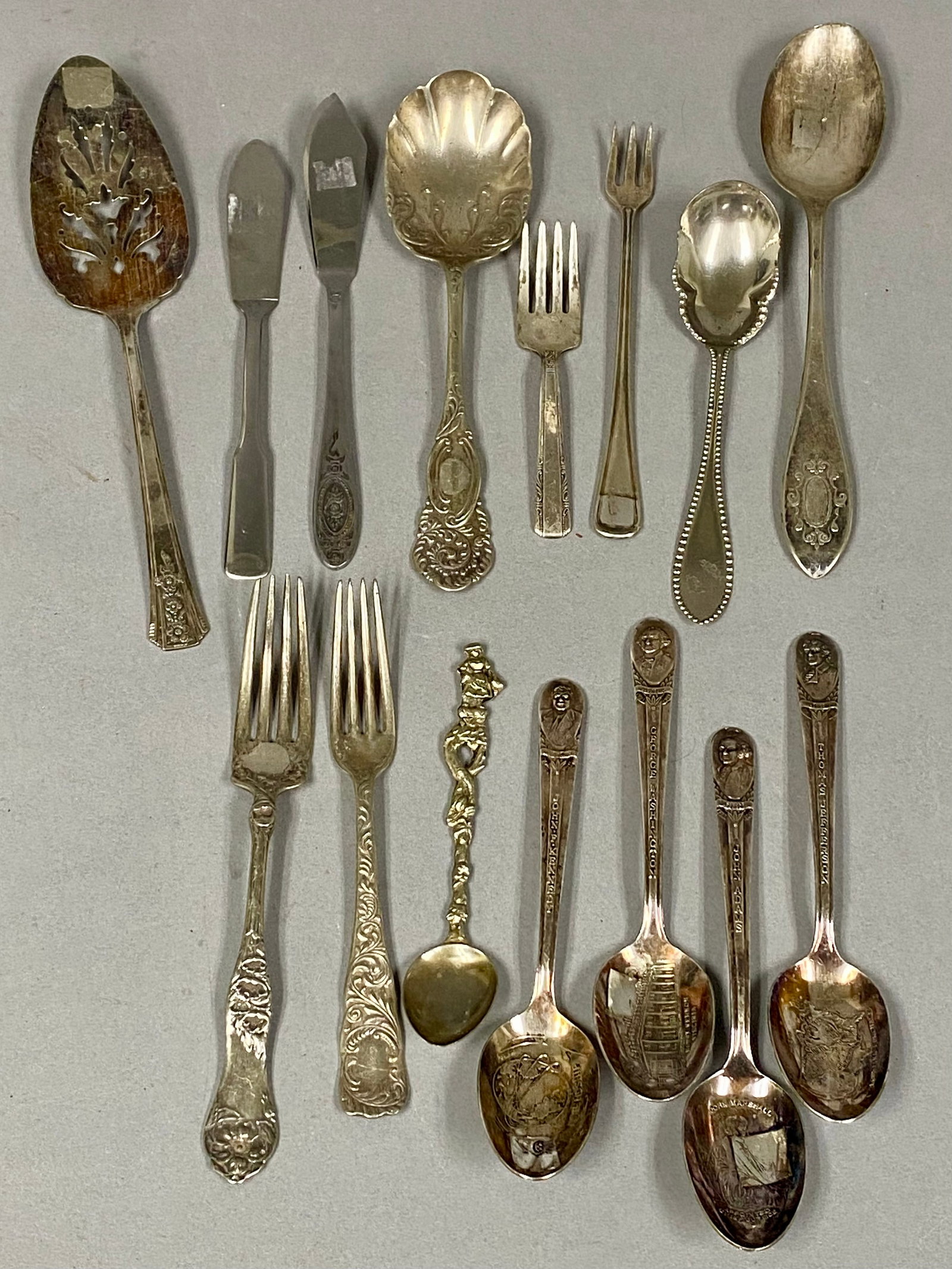 Collection of 17 Silverplated Flatware Pieces: This assortment of 17 silverplated flatware pieces includes commemorative spoons, serving items, and place setting forks marked by manufacturers such as Wm. Rogers, Oneida, Wallace, and Rockford.