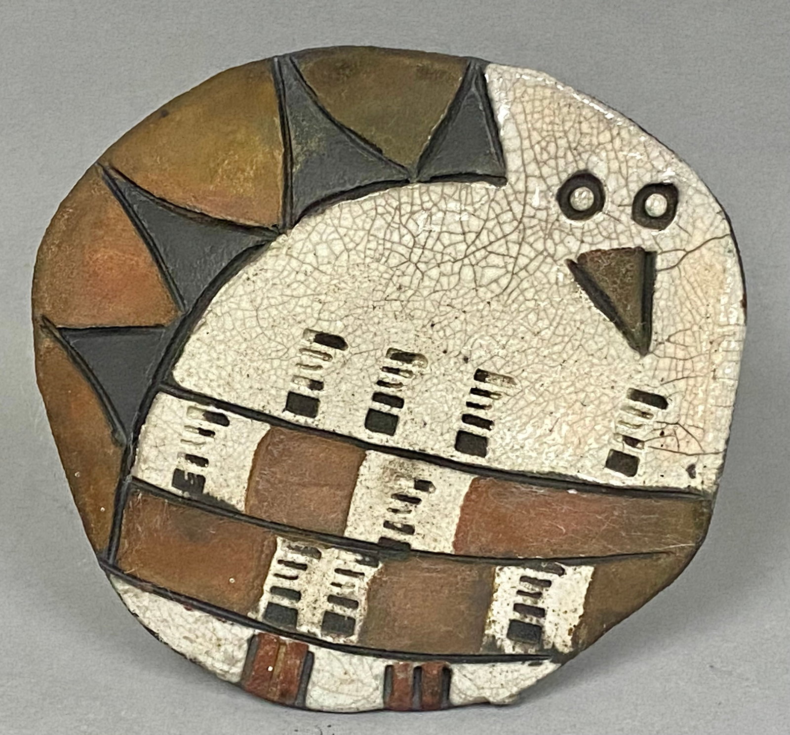Jordy Studio Pottery Owl Plaque: This ovid studio pottery wall plaque is by the workshop of Einar and Bess Jordy. The stoneware piece features a stylized bird motif set against a geometric background, rendered with a combination of