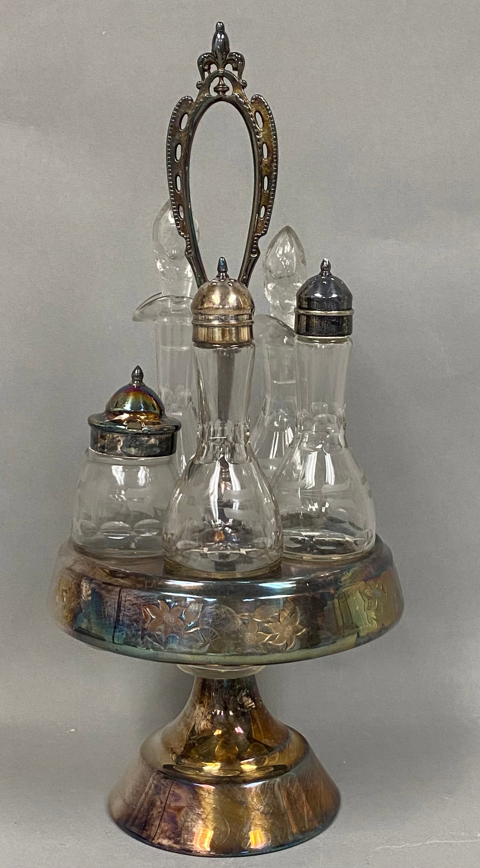Aurora Silver Plate Cruet Set: An Aurora Silver Plate Manufacturing Company Victorian-style rotating caster set featuring a triple-plated stand and a collection of five etched glass bottles. The stand is decorated with floral engra