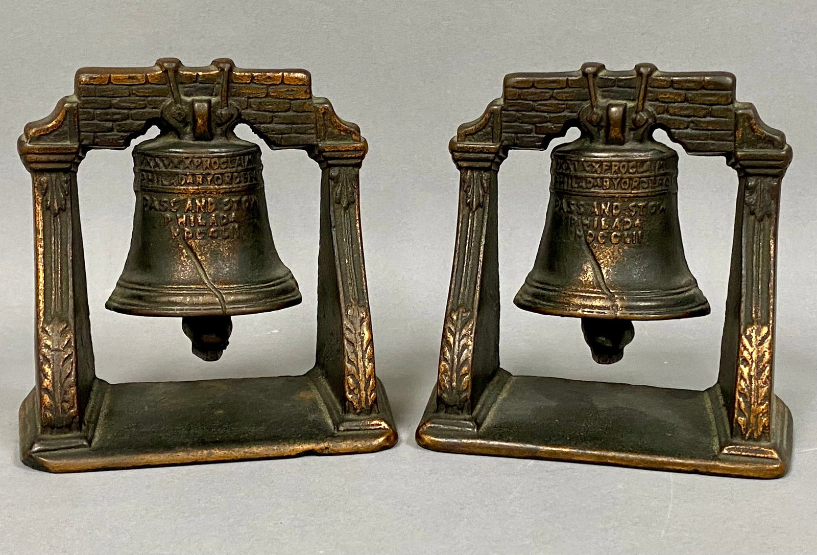 A Pair of Cast Iron Liberty Bell Bookends: A pair of cast iron bookends featuring a relief representation of the Liberty Bell within a classical architectural frame. The frames are designed with a brick-patterned lintel supported by