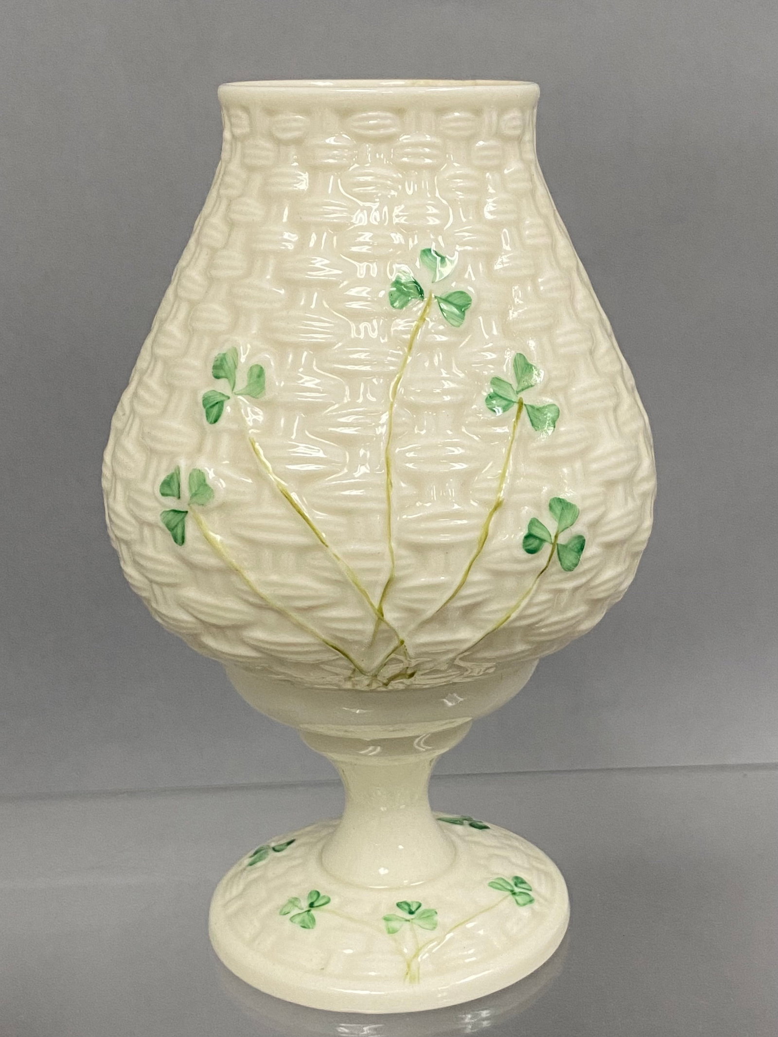 Belleek Shamrock Basketweave Fairy Lamp: A two-part Parian porcelain fairy lamp by Belleek featuring a molded basketweave texture and hand-painted shamrocks. The piece consists of a bulbous globe that rests upon a matching circular pedestal