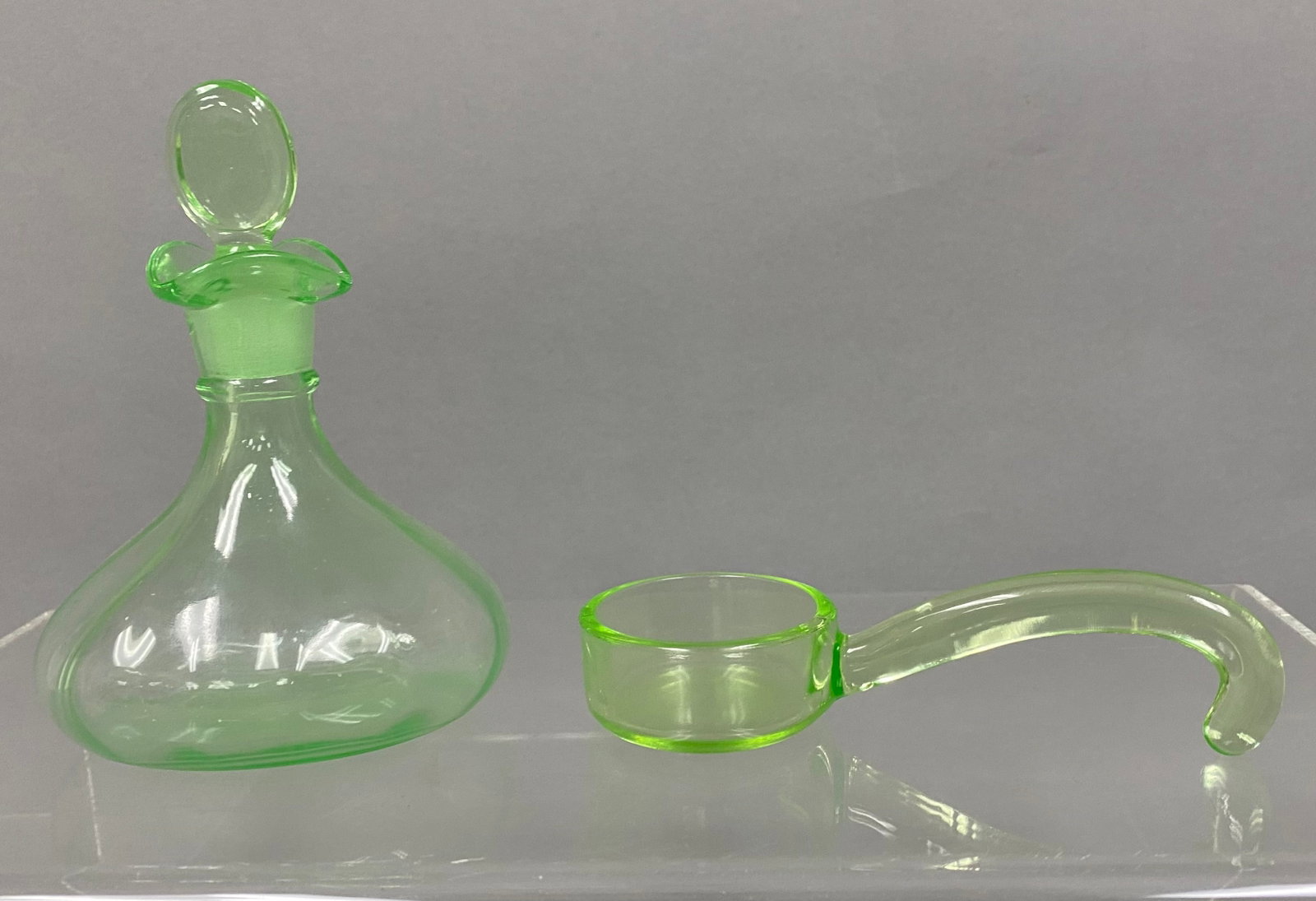 Two Uranium Glass Serving Pieces: This lot comprises a mold-blown uranium glass cruet and a handled ladle. The cruet features optic ribbing, a ruffled rim, and a ground-glass stopper with a circular finial. Both items exhibit a strong