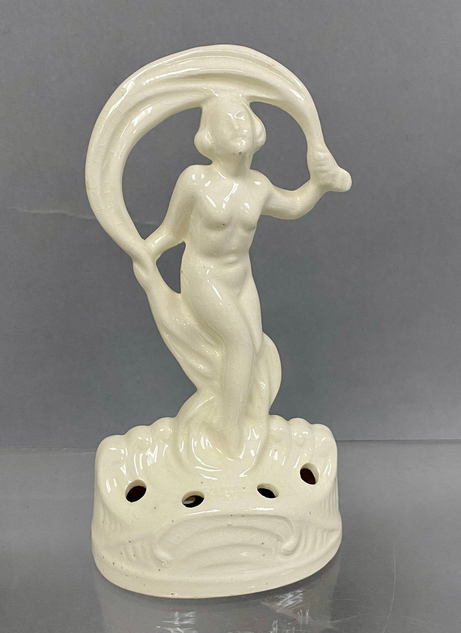 Coronet Germany Art Deco Flower Frog: This glazed porcelain flower frog features a nude female figure draped in a stylized scarf standing on a wave-form base. The base is pierced with eight circular holes for floral stems and bears a brow