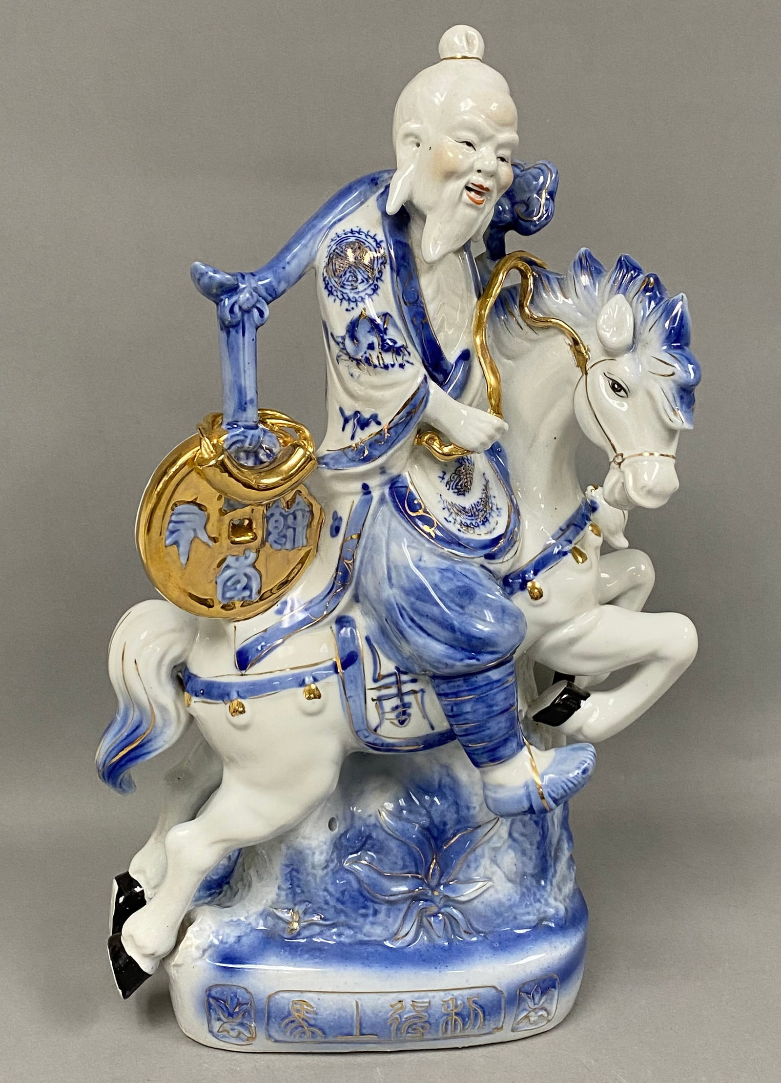 Chinese Gilt Porcelain Sage Riding Horse: This glazed porcelain figurine depicts an elderly immortal riding a caparisoned horse while holding a staff with a fish and a large coin. The decoration includes underglaze blue, polychrome enamels