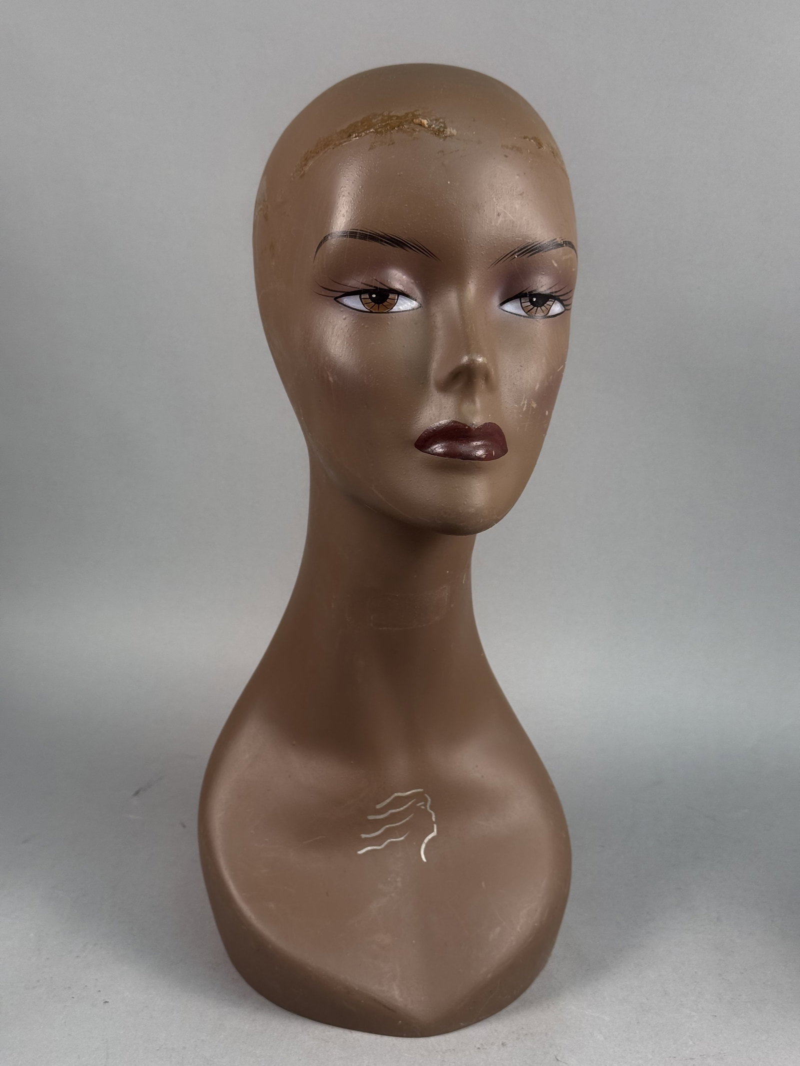 Stylized Molded Plastic Mannequin Head Bust: A vintage female mannequin display bust crafted from molded plastic with a matte brown finish. The head features stylized facial features including arched eyebrows, defined eyeliner, and dark-toned li