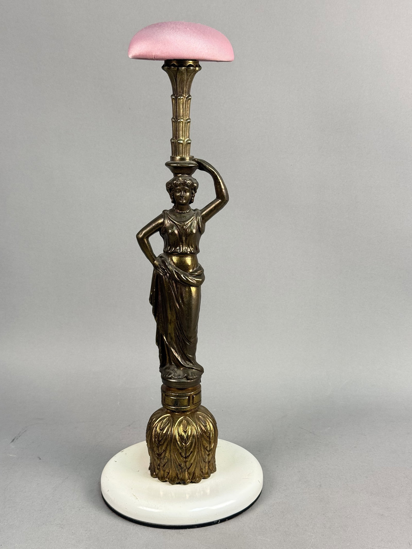 Brass-Toned Metal Caryatid Hat Stand: This neoclassical-style millinery hat stand features a cast-metal figurine of a woman in classical draped attire, posed as a caryatid. The figure stands with one hand on her hip while the other arm