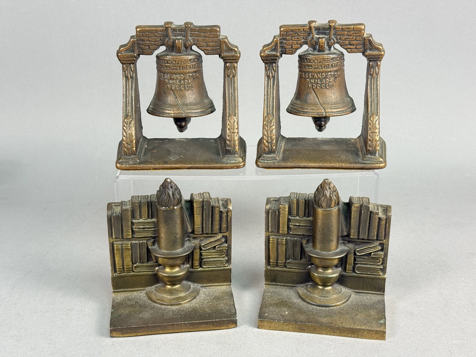 Philadelphia Mfg. Co. Plated Metal Bookends: An assortment of two pairs of vintage decorative bookends produced by the Philadelphia Mfg. Co. One pair features a three-dimensional representation of the Liberty Bell suspended within a brickwork ar