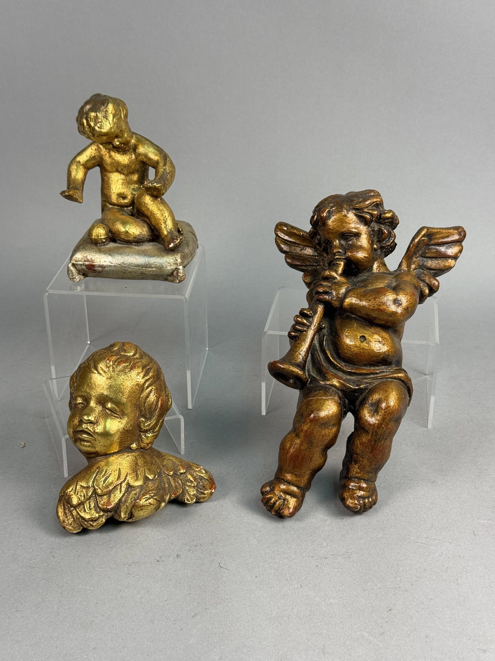 Nettle Creek & World Art Gilt Cherubs: A trio of decorative cherub figurines including a seated figure on a silver-toned cushion, a winged wall-hanging figure playing a trumpet, and a winged cherub head. The trumpet-playing cherub