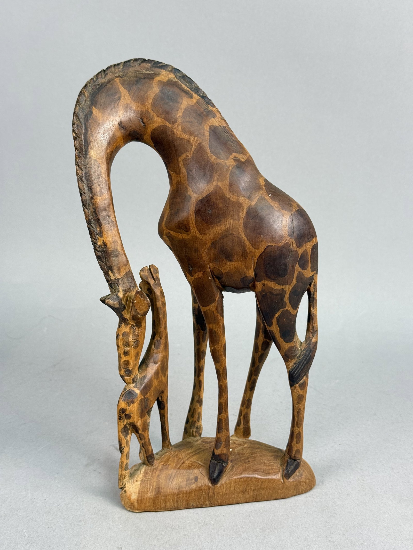 Kenyan Wood Arched-Neck Giraffe Sculpture: A Kenyan hand-carved wooden sculpture depicting a mother giraffe and her calf on an integrated base. The mother is rendered in a stylized arched-neck pose, bending toward the smaller calf positioned