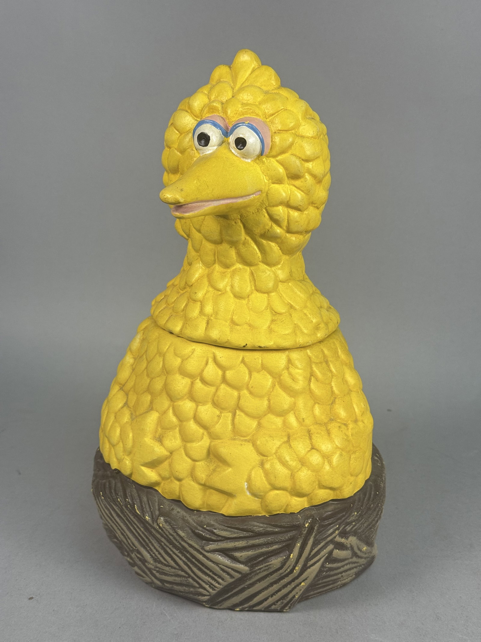 Muppets Inc Ceramic Big Bird Cookie Jar: A vintage two-part ceramic cookie jar depicting the Sesame Street character Big Bird. The piece consists of a removable lid formed by the head and neck, which rests on a body section depicting the cha