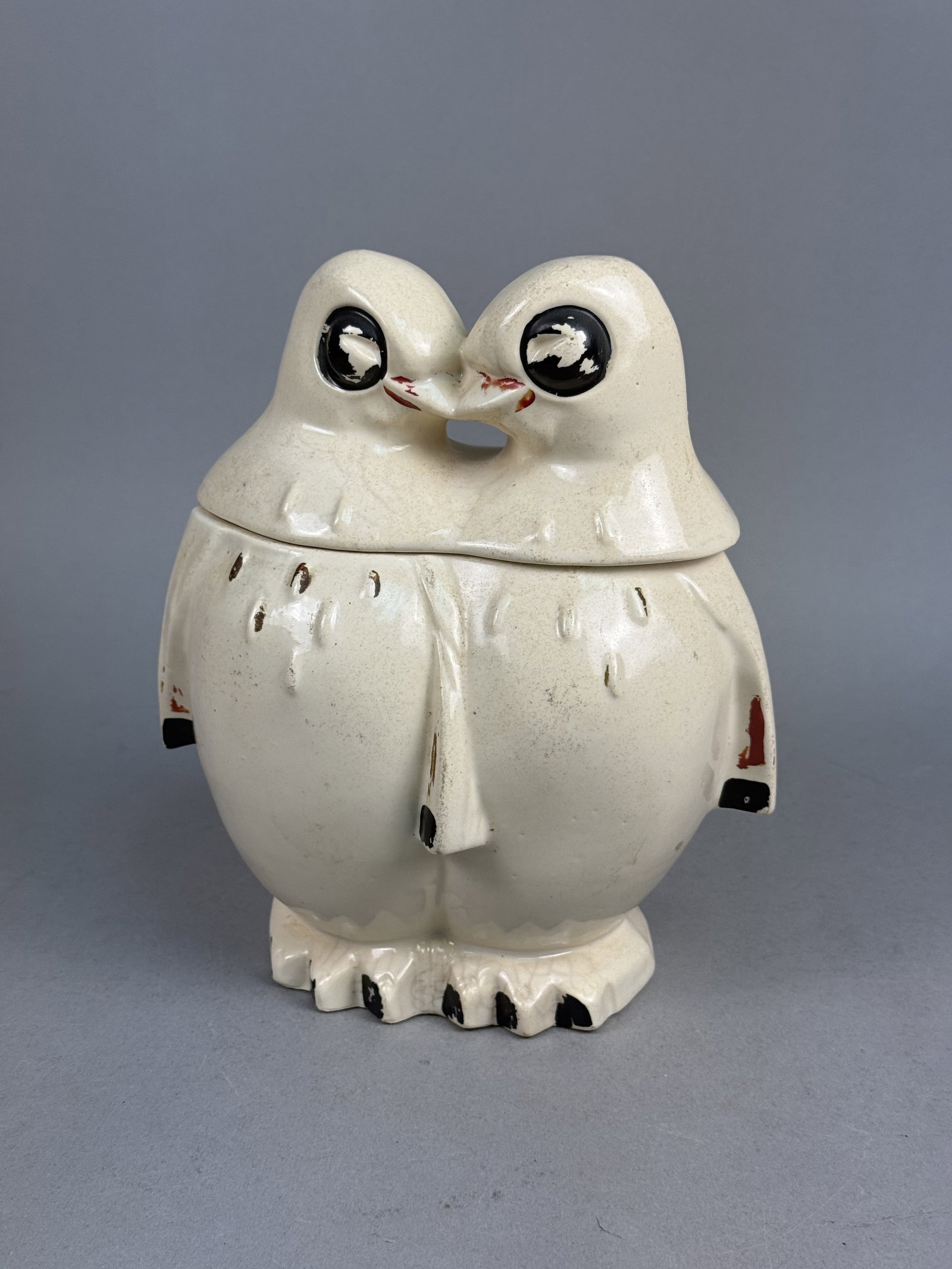 Earthenware Nuzzling Penguin Cookie Jar: This mid-century lidded earthenware cookie jar is designed in the form of two stylized, nuzzling penguins. The two-piece vessel features a lid comprising the joined heads and shoulders of the