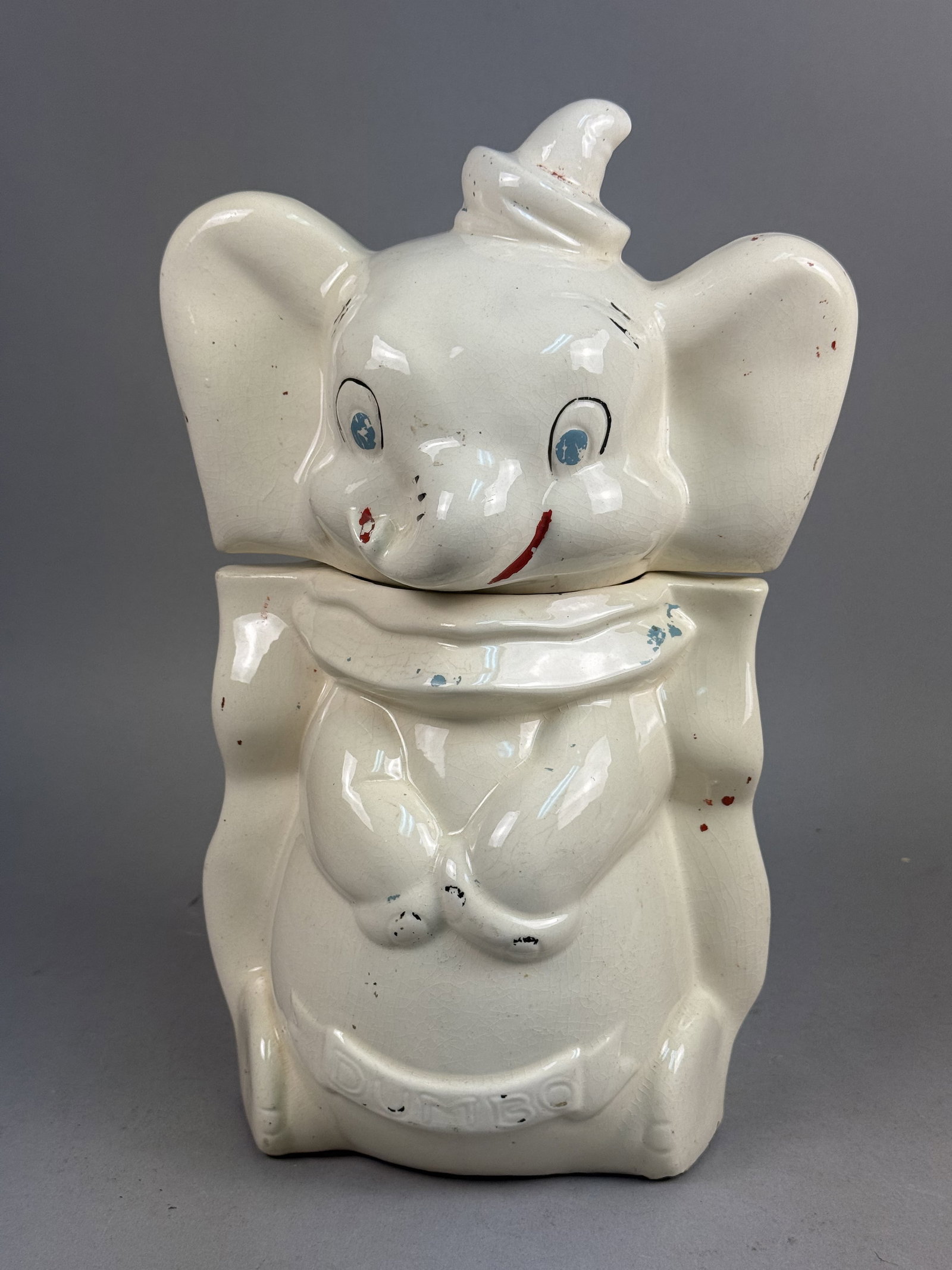 Walt Disney Productions Ceramic Turnabout Dumbo Cookie Jar: This vintage glazed ceramic cookie jar features the Disney character Dumbo in a turnabout design, presenting two distinct facial expressions and poses on opposite sides. The front of the jar includes 