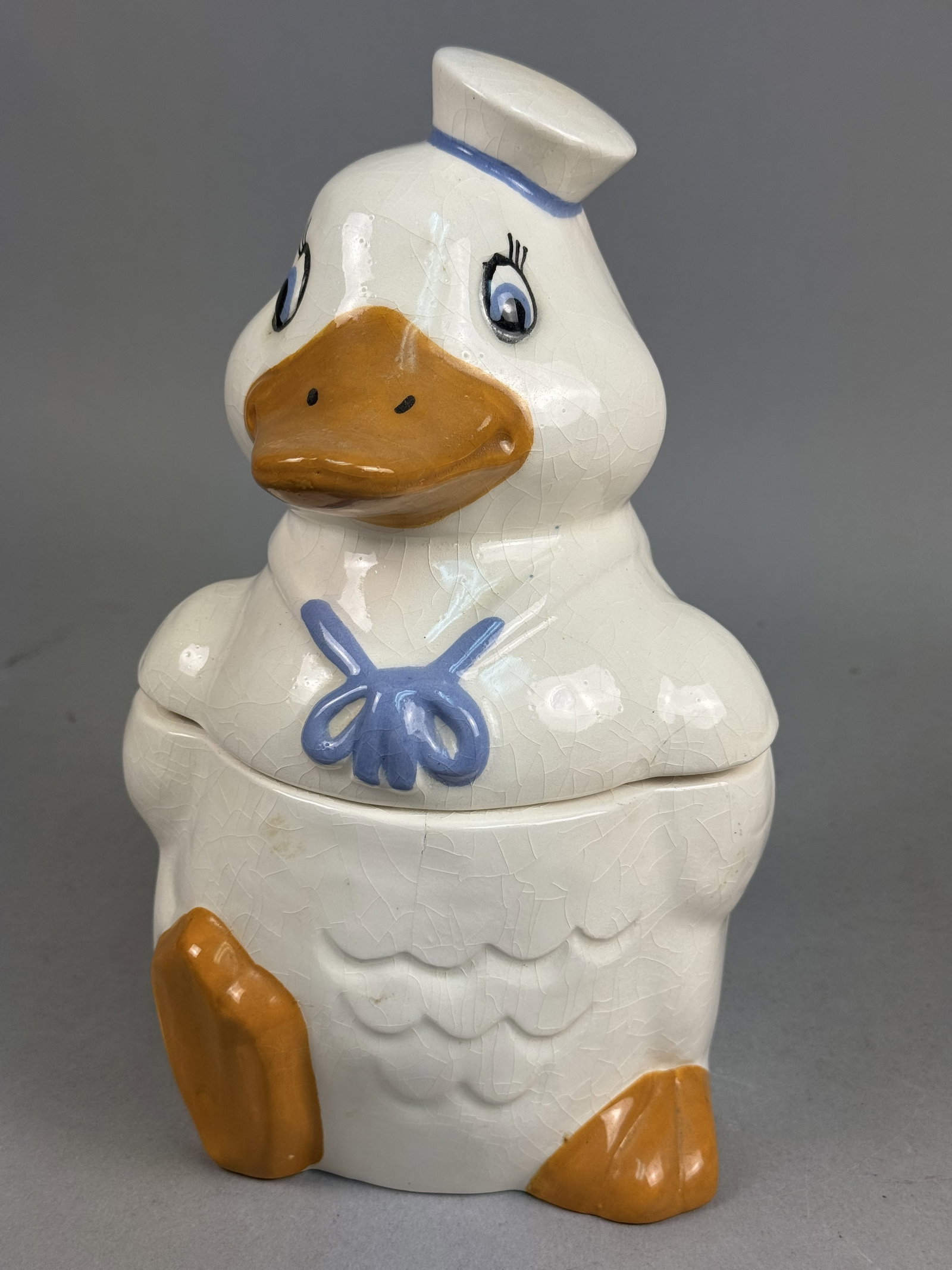 Earthenware Sailor Duck Cookie Jar: A mid-century figural cookie jar modeled as an anthropomorphic sailor duck. The two-piece earthenware vessel features a cream-colored glazed finish with hand-painted decorative accents. The duck is