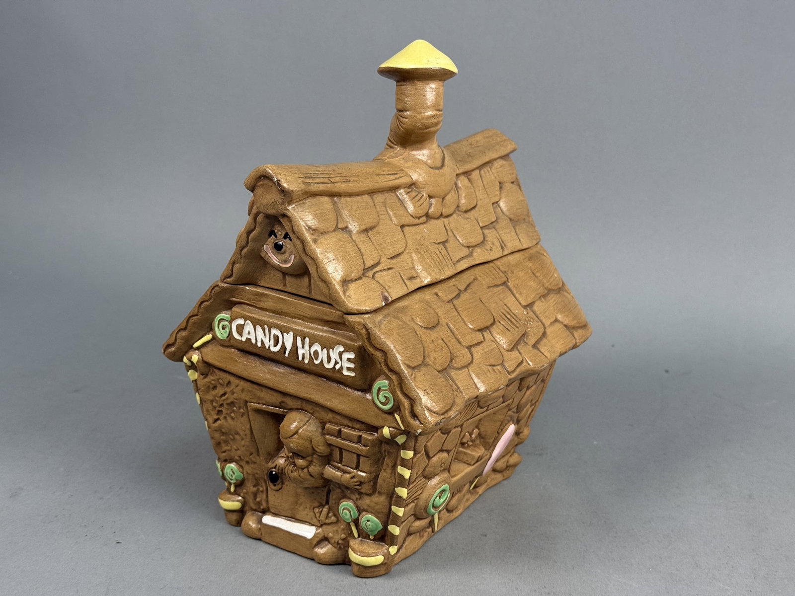 Candy House Ceramic Gingerbread Jar: A two-piece ceramic storage jar modeled as a whimsical gingerbread cottage with a textured, matte-finished brown exterior. The relief-molded decoration features shingled roof tiles, timber framing,