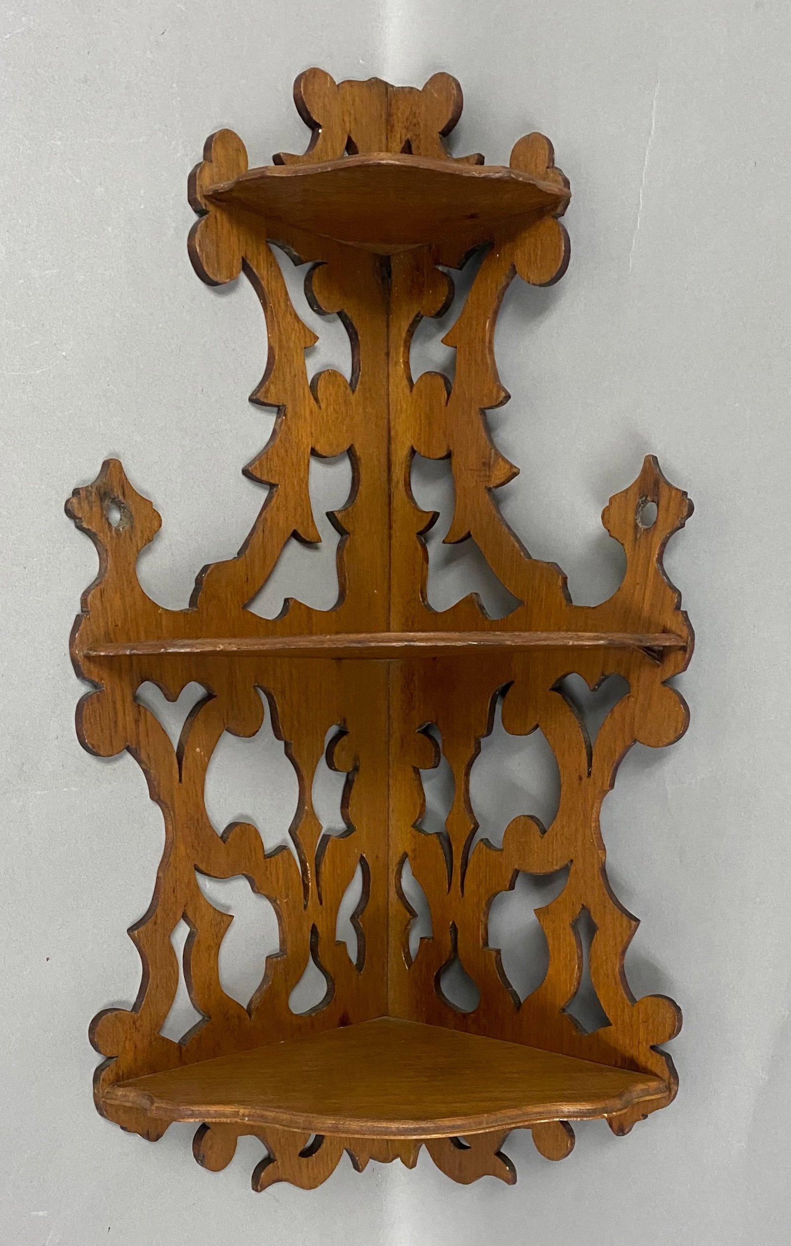 Victorian Three-Tier Fretwork Corner Shelf: This Victorian style corner shelf is constructed of wood with a dark stain and features elaborate scroll-sawn fretwork with foliate and fleur-de-lis motifs. The three-tier design includes graduated
