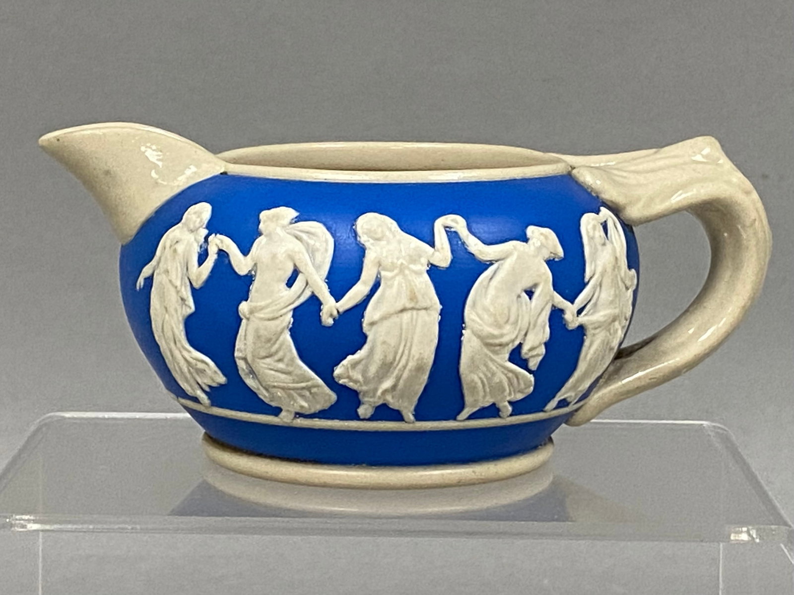 Spode Marlborough-Blenheim Blue Sprigware Creamer: This Spode Copeland sprigware creamer in blue stoneware features the classical Dancing Hours bas-relief pattern. The vessel is decorated with applied white figures and finished with a cream-glazed