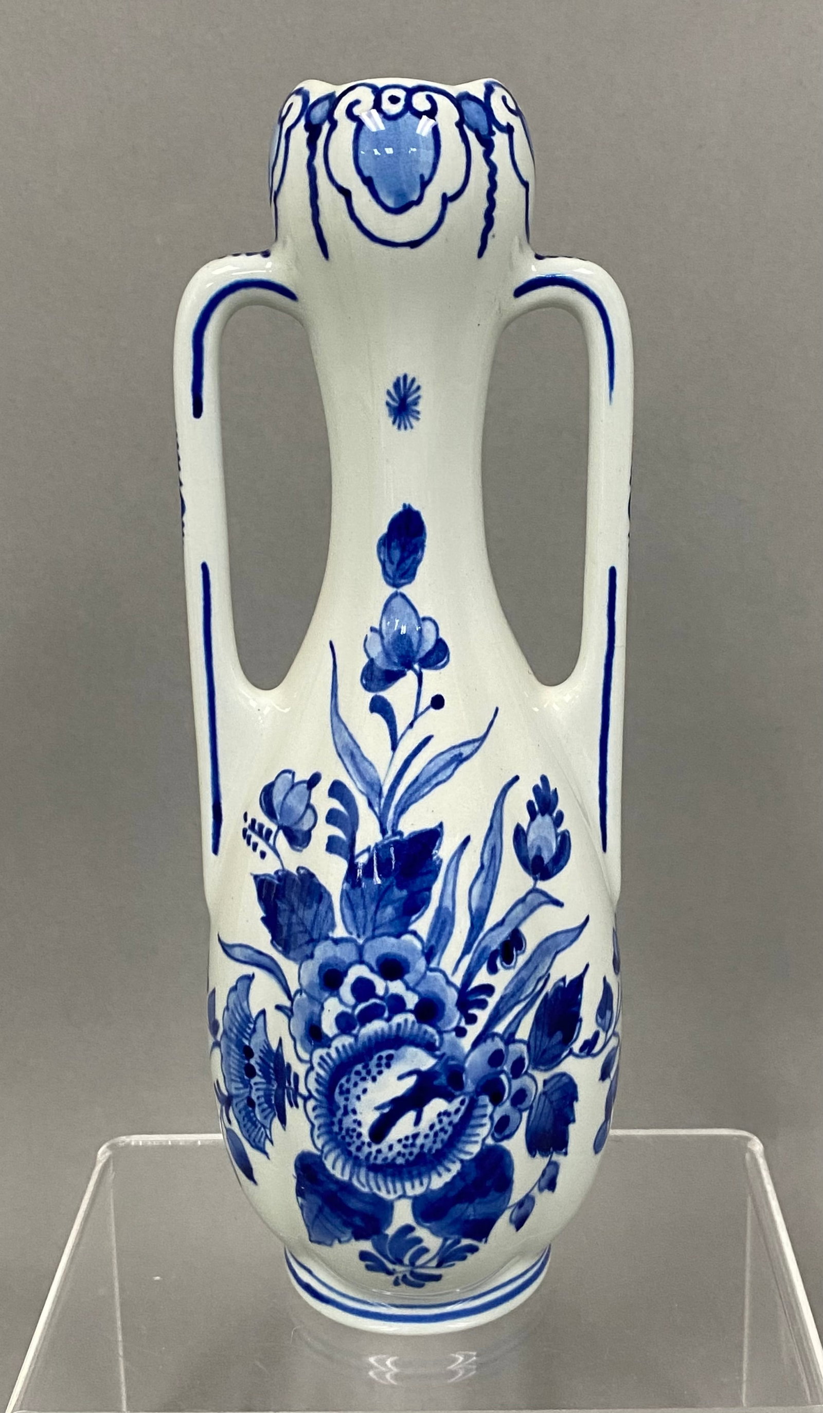 Royal Delft Hand-Painted Handled Vase: This Royal Delft (De Porceleyne Fles) double-handled vase is crafted from glazed earthenware and decorated with hand-painted underglaze blue floral motifs. The bulbous body features a central blossom