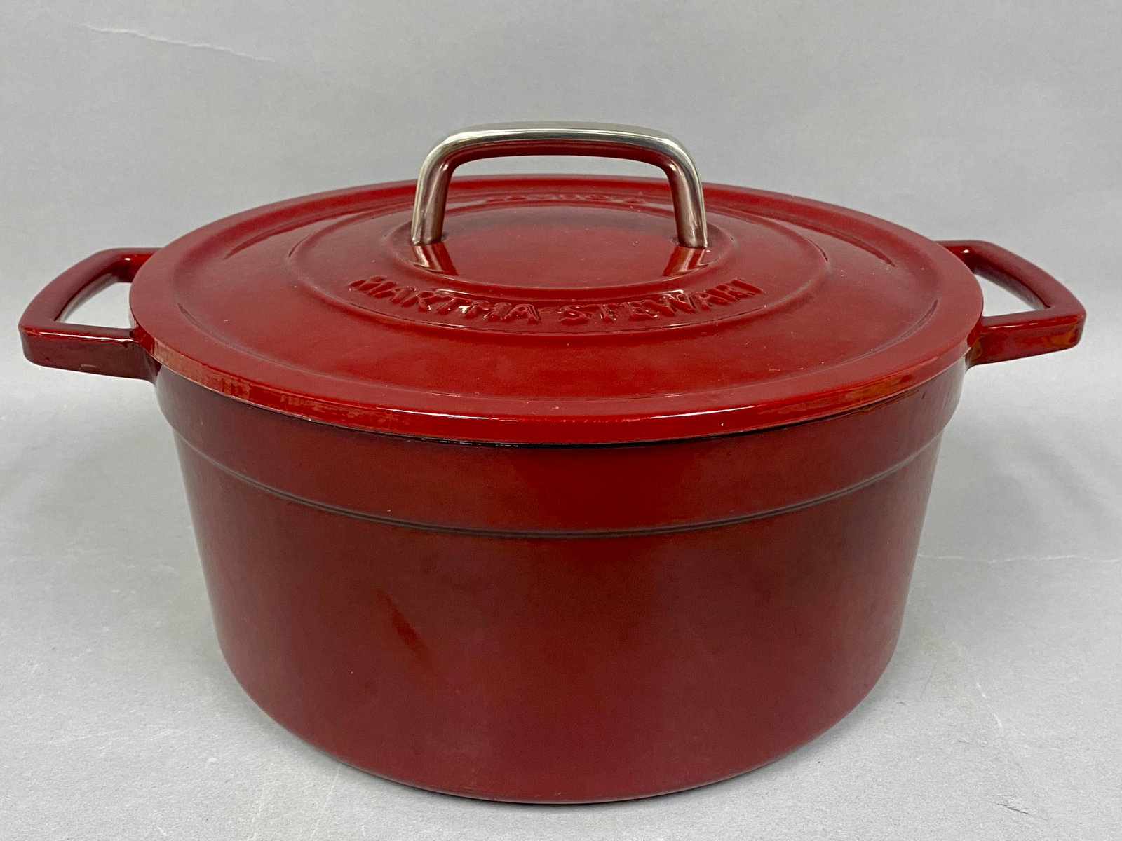 Martha Stewart 6-Quart Enameled Dutch Oven: A Martha Stewart 6-quart Dutch oven constructed from enameled cast iron with a glossy red exterior and a cream interior. The matching lid is embossed with the maker's name and capacity and features a