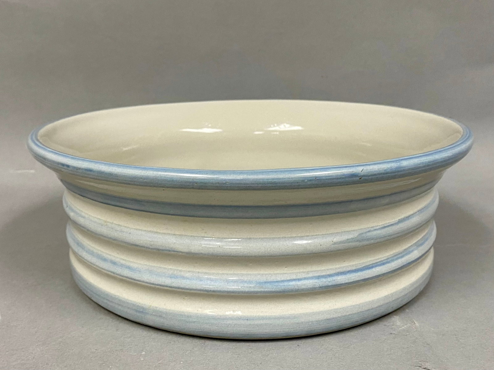 Louisville Stoneware Blue Banded Bowl: This round serving bowl is produced by Louisville Stoneware in Kentucky. It features a cream glaze accented by hand-applied light blue bands on the rim and five exterior ridges. The base is stamped