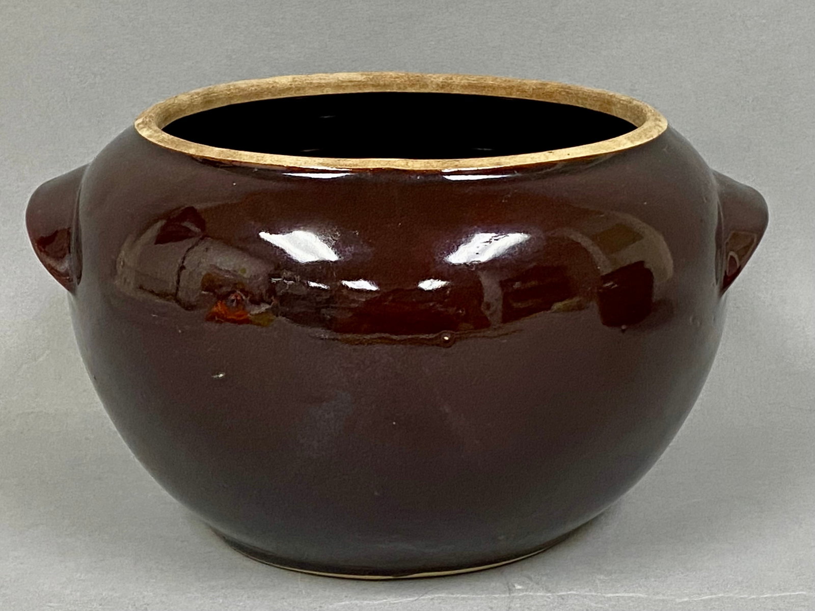 American Glazed Stoneware Bean Pot: A round American stoneware bean pot featuring a deep brown high-gloss glaze and two integrated tab-style handles. The piece is designed with a tapered neck and a wide opening, revealing a light tan